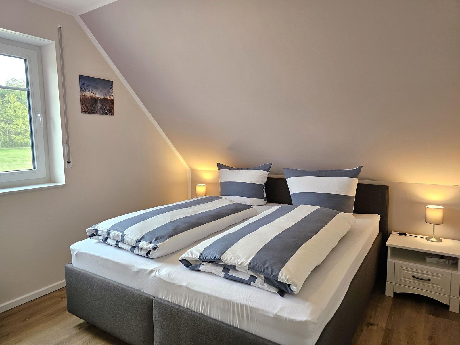 Schlafzimmer mit Doppelbett, Fenster und Nachttisch.