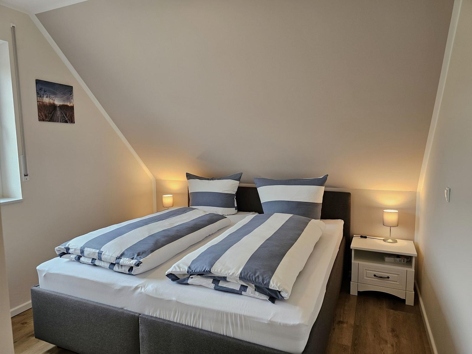 Schlafzimmer mit Doppelbett, Nachttisch und Stehlampe unter schräger Decke.