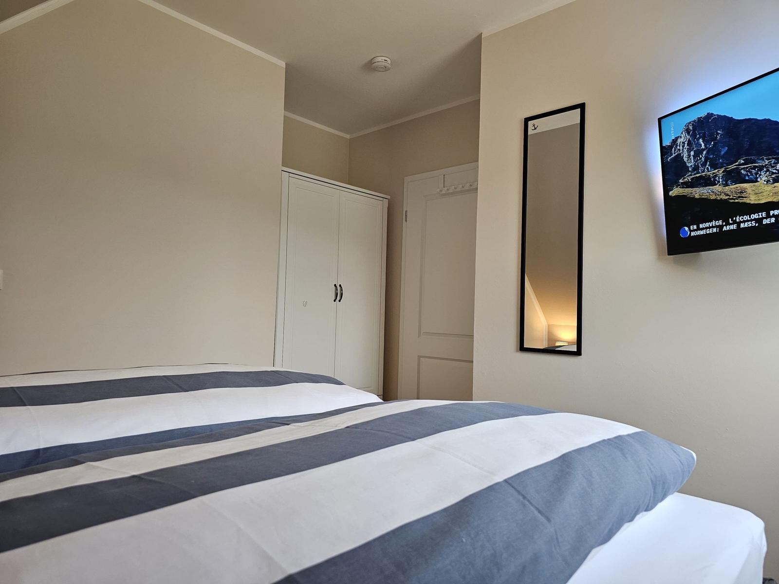 Schlafzimmer mit Bett, Kleiderschrank und Wandspiegel. Fernseher an der Wand.
