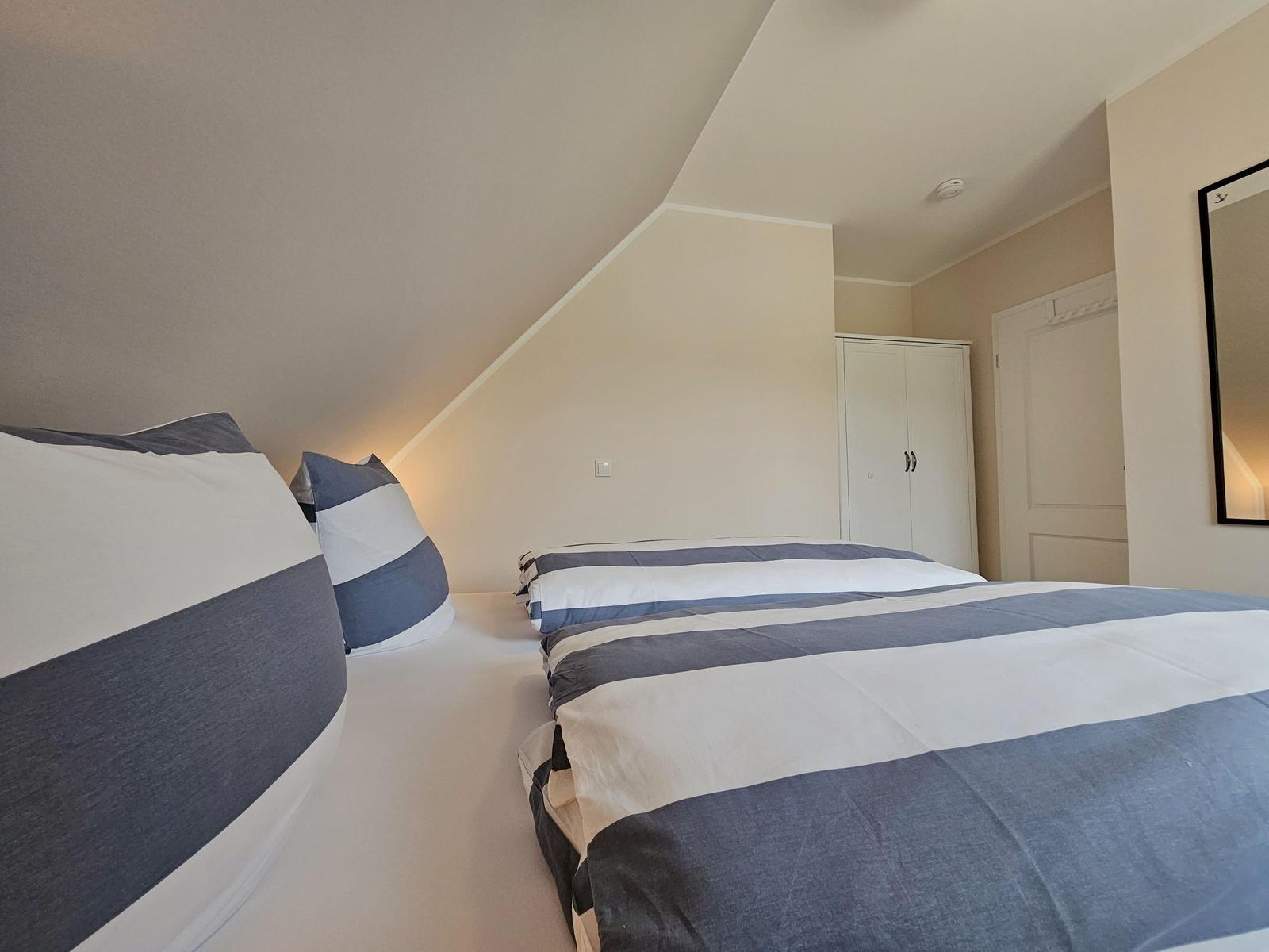 Schlafzimmer mit Doppelbett, Kleiderschrank und Spiegel an der Wand.