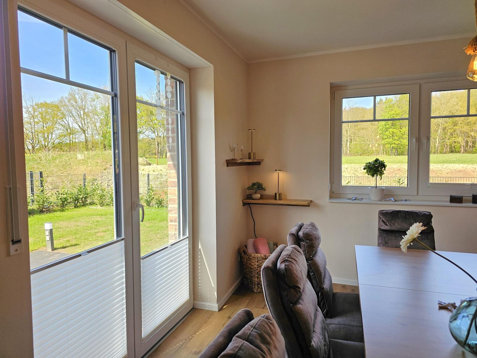 Essbereich mit Tisch, Stühlen und Blick auf Garten. Fenster und Tür mit Blick auf Grün.