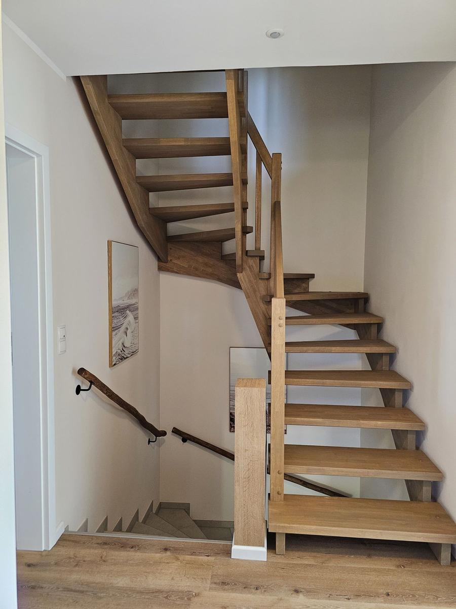 Holztreppe mit Geländer führt zur oberen Etage. Wandbild und Lichtschalter sichtbar.