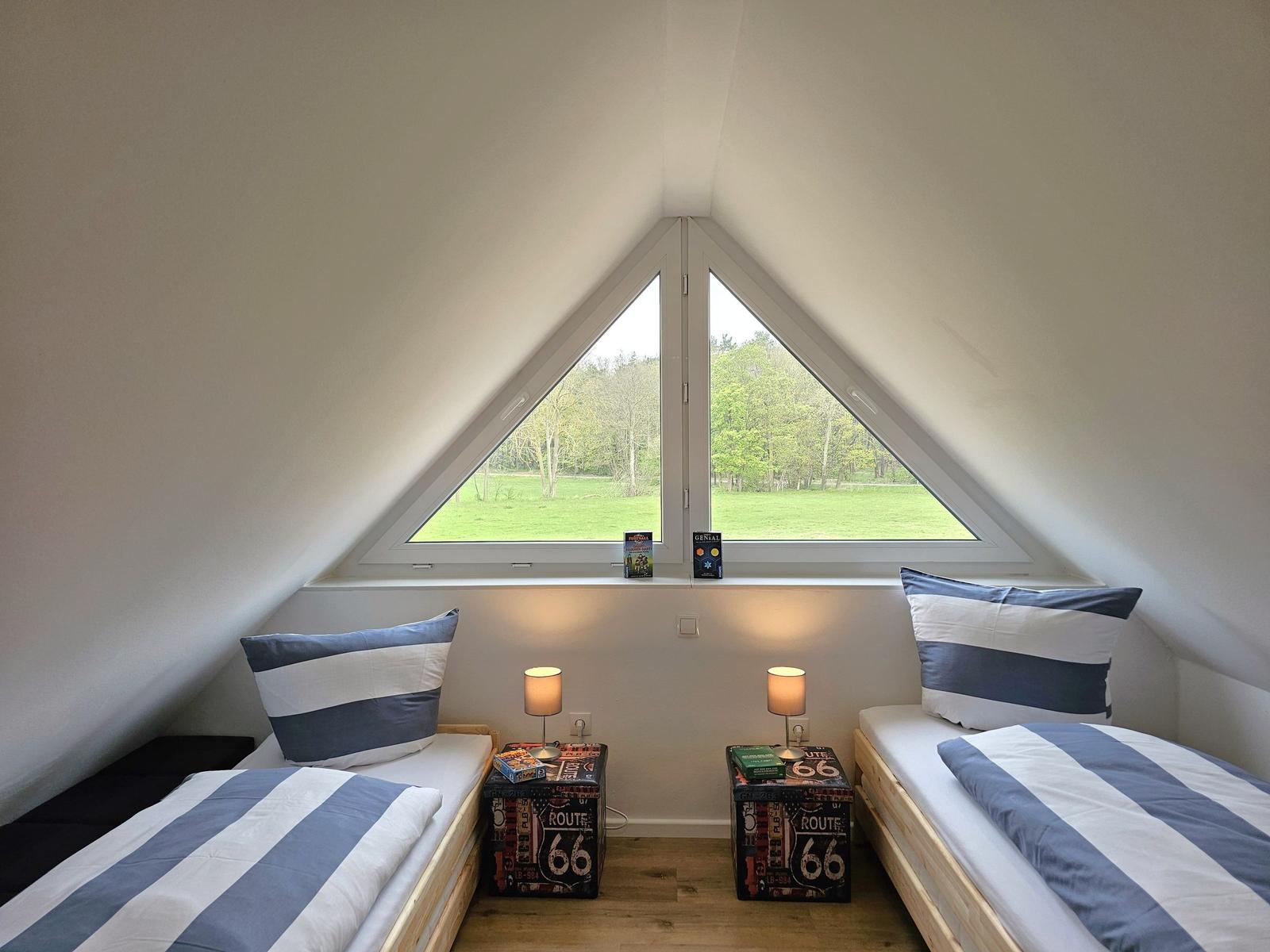 Zwei Betten unter einem Dachfenster mit Blick auf einen grünen Garten.