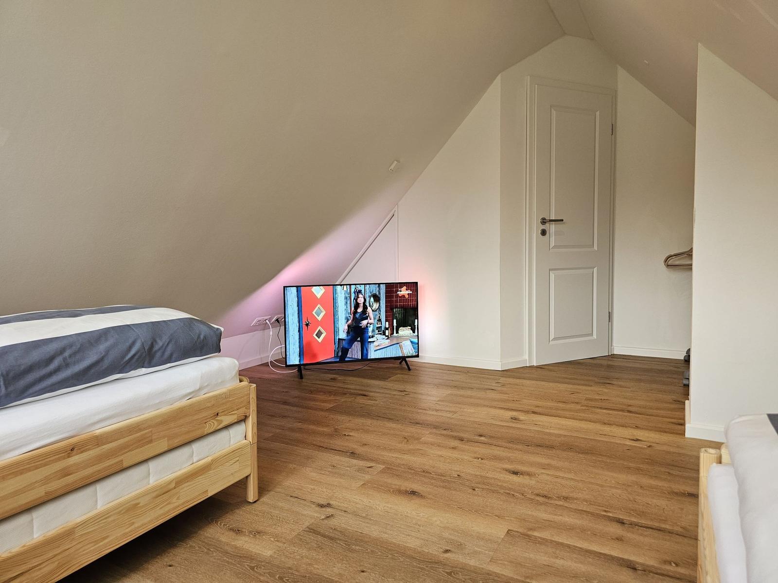 Schlafzimmer mit Dachschrägen, Holzboden und Fernseher.