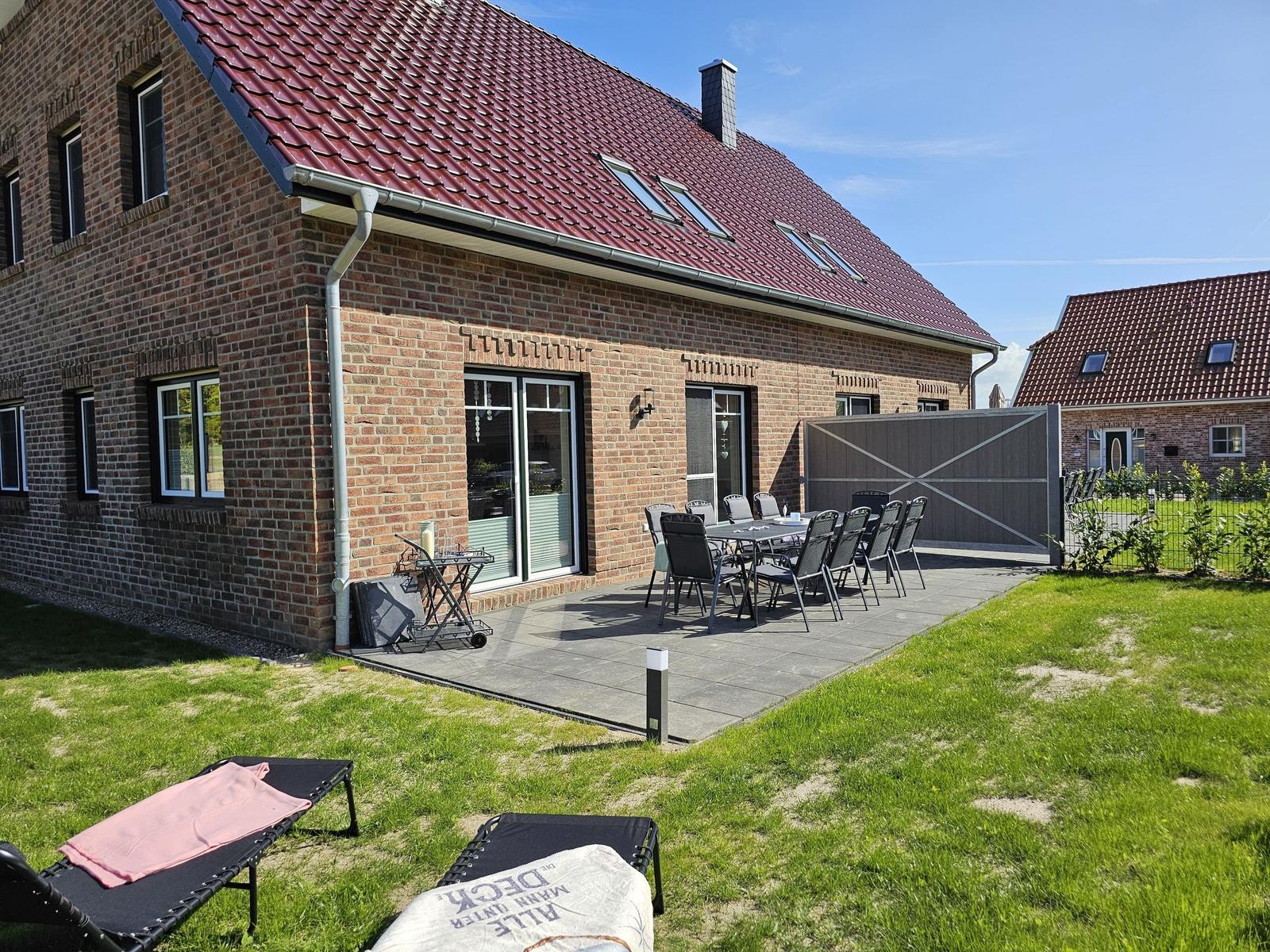 Haus mit Terrasse, Garten und Liegen. Tisch und Stühle stehen bereit.