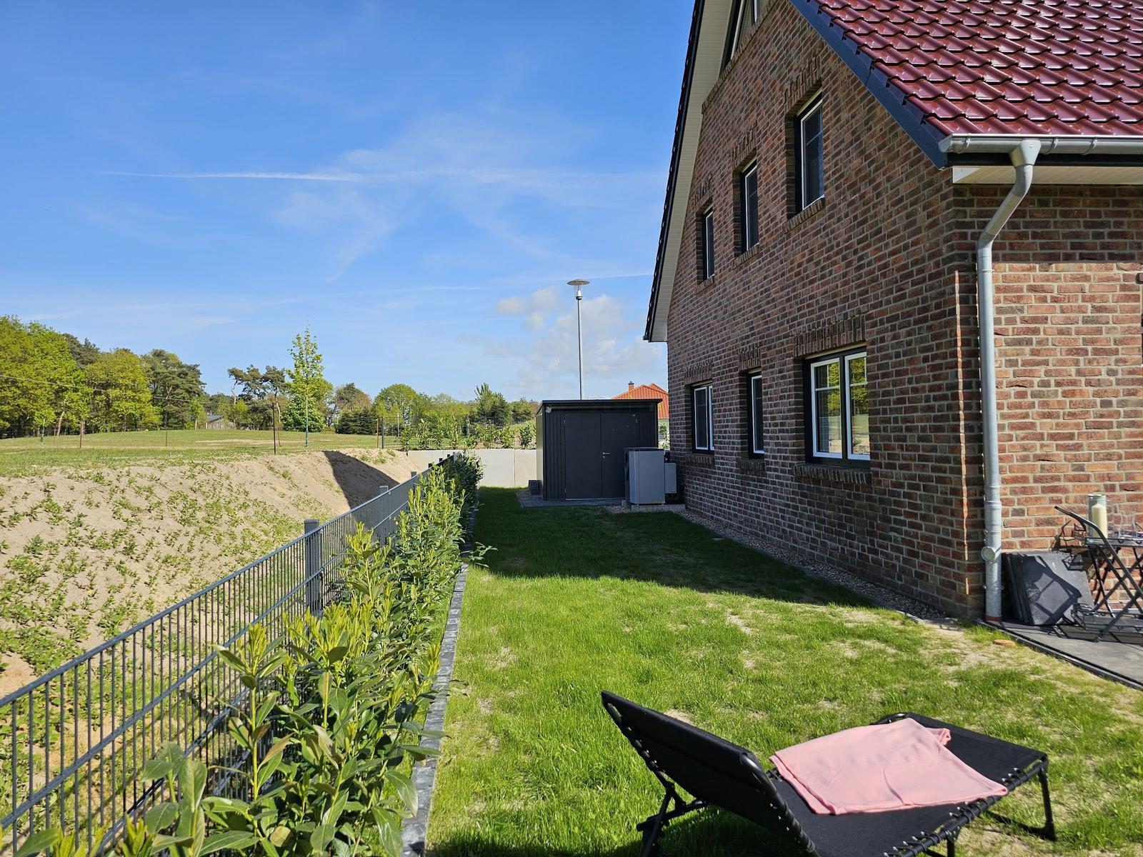 Hinterhof mit Liegestuhl, Grasfläche und Backsteinhaus unter blauem Himmel.