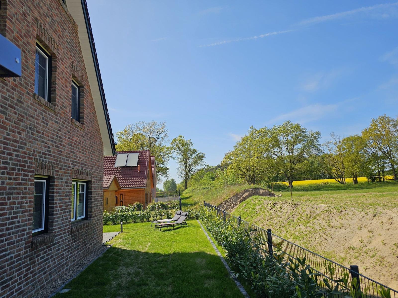 Haus mit Garten, Sonnenliegen und Blick auf Felder und Bäume.