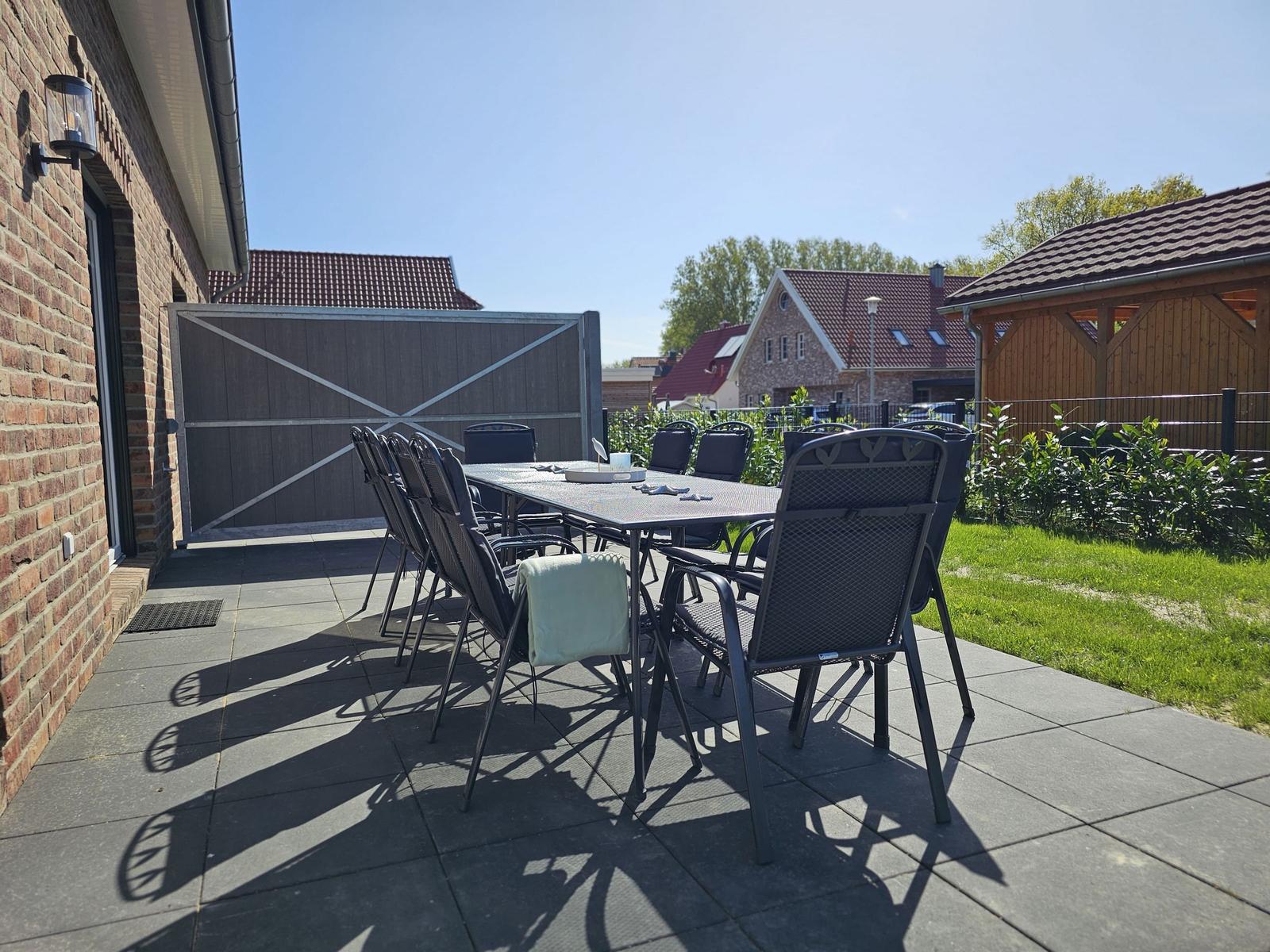 Terrasse mit Tisch und Stühlen neben Haus mit Garten.