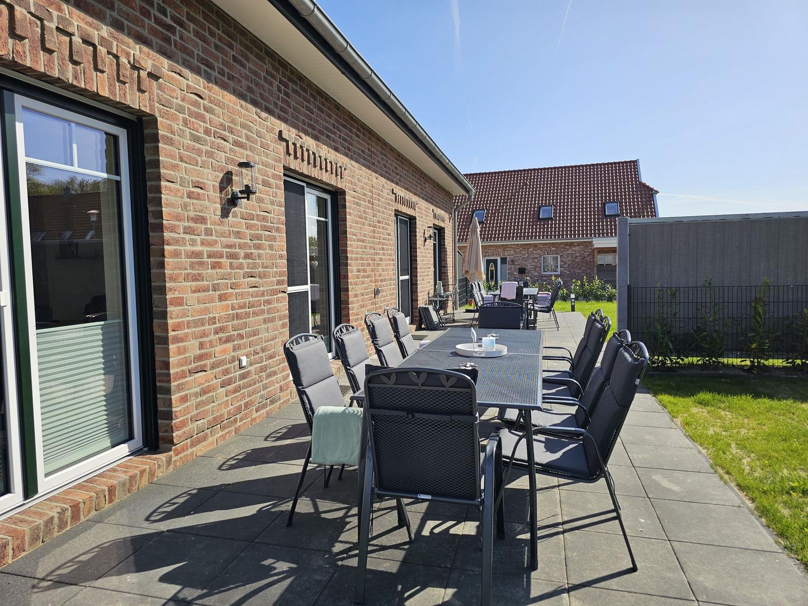 Terrasse mit Sitzgruppe und Garten. Hauswand aus Backstein. Hinterhof mit Zaun.
