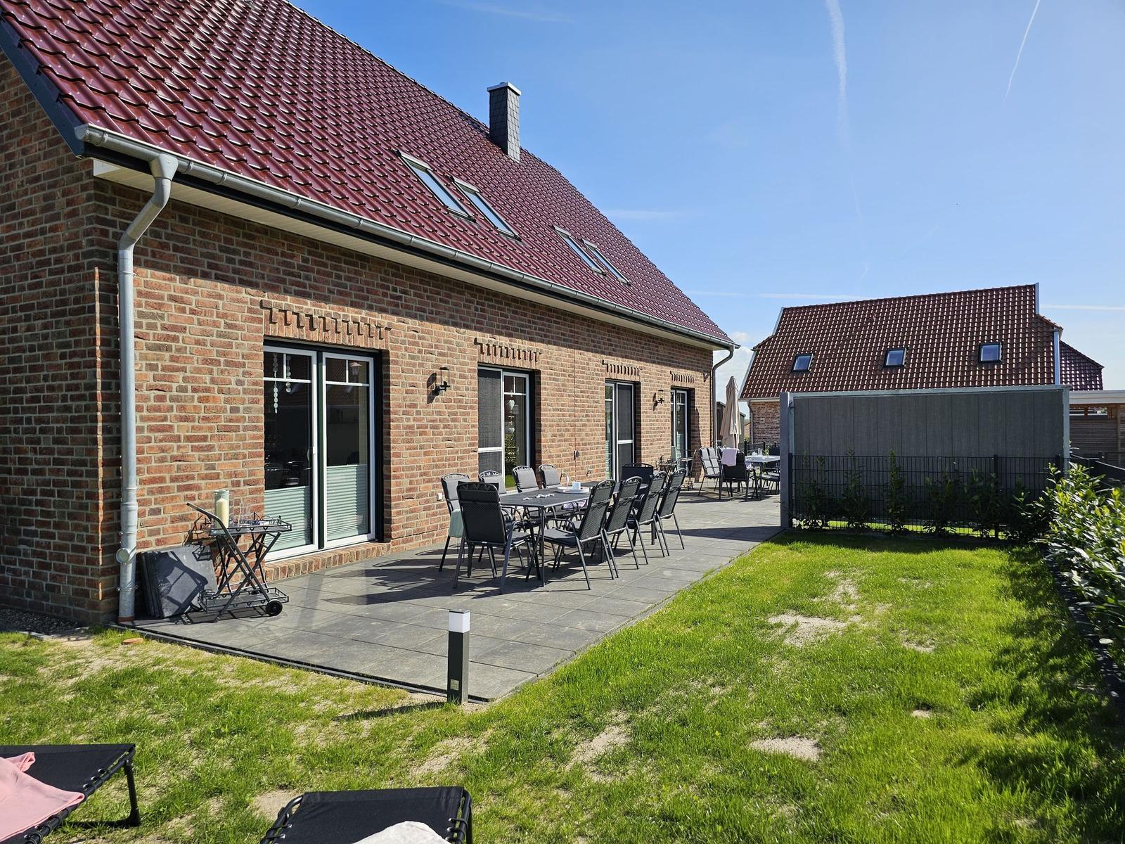 Haus mit Terrasse, Garten und Sitzgelegenheiten. Dach mit Dachfenstern.