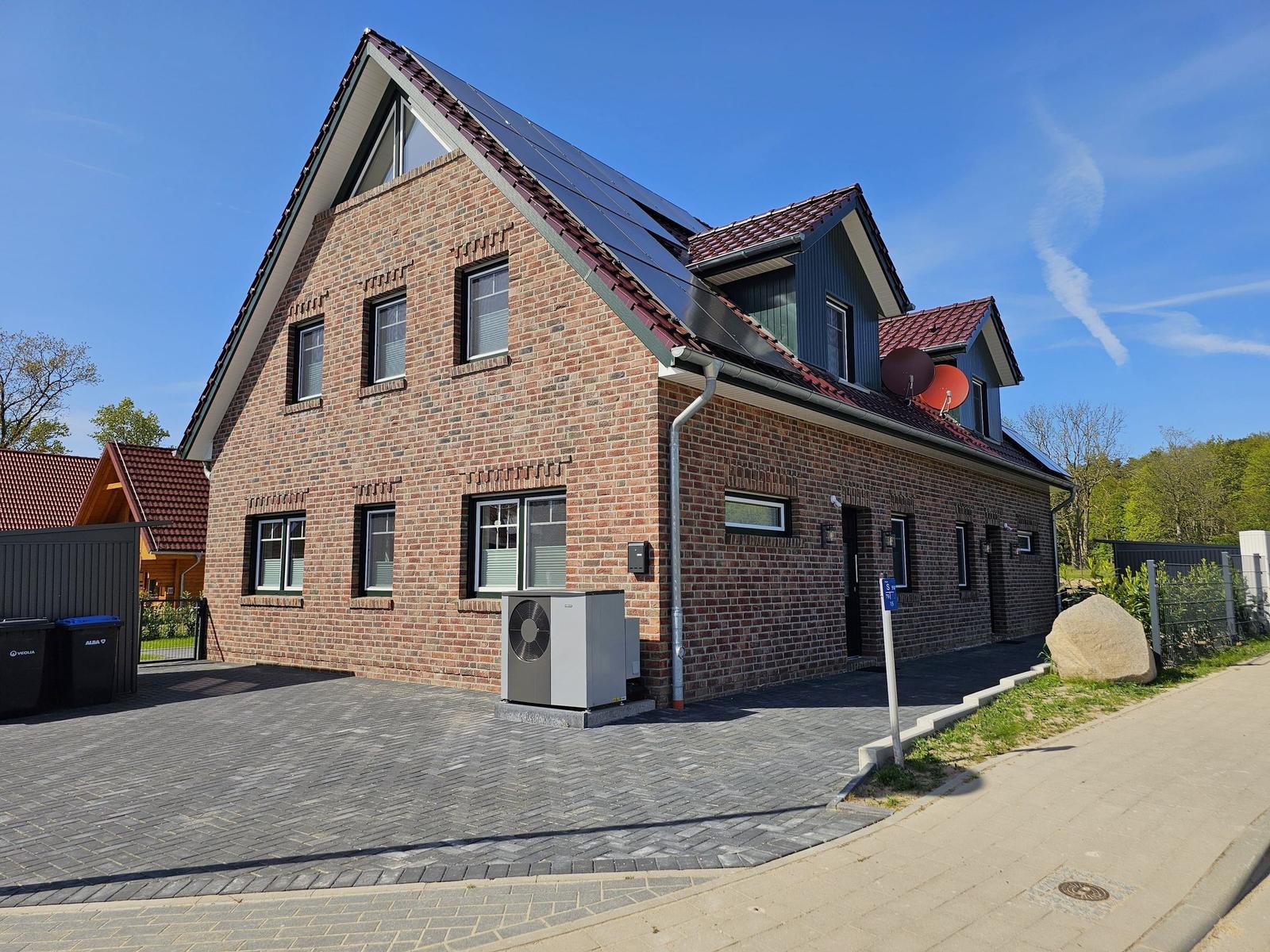 Zweistöckiges Haus mit Solaranlage und Dachgauben. Vorhof mit Pflastersteinen und Satellitenschüsseln.