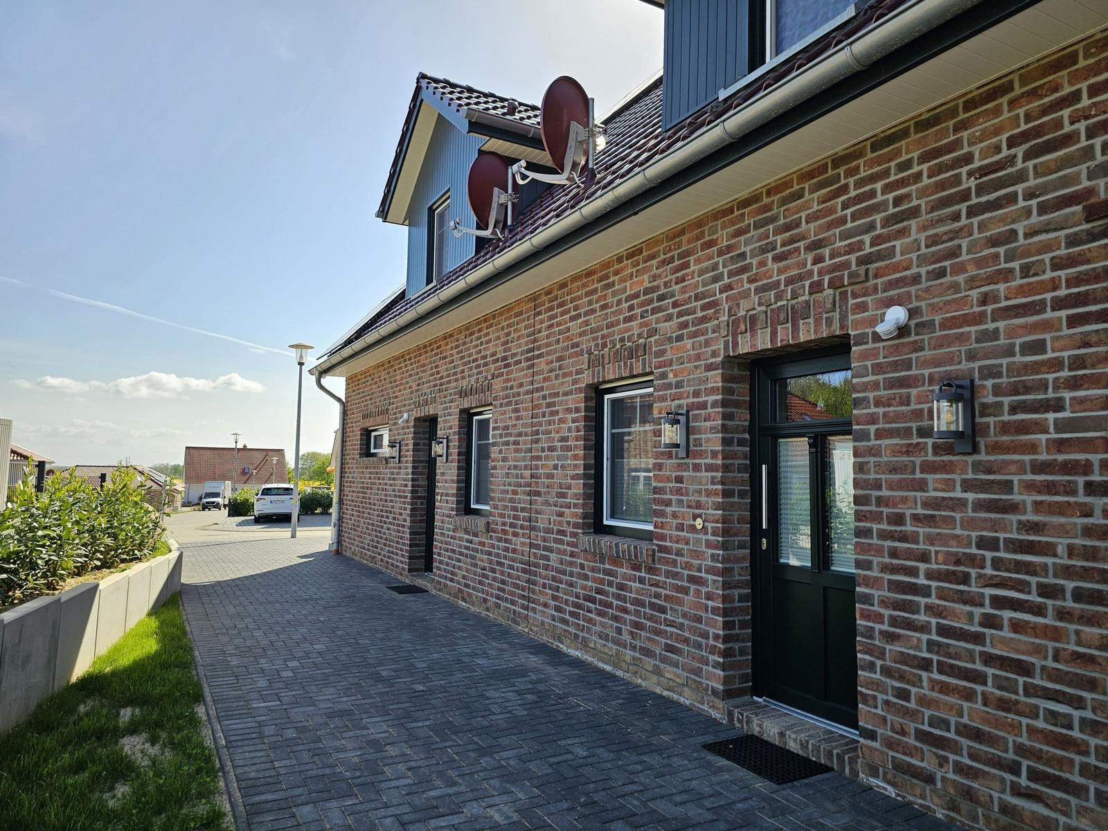 Haus mit Backsteinfassade, Eingangstür und Satellitenschüsseln auf dem Dach.