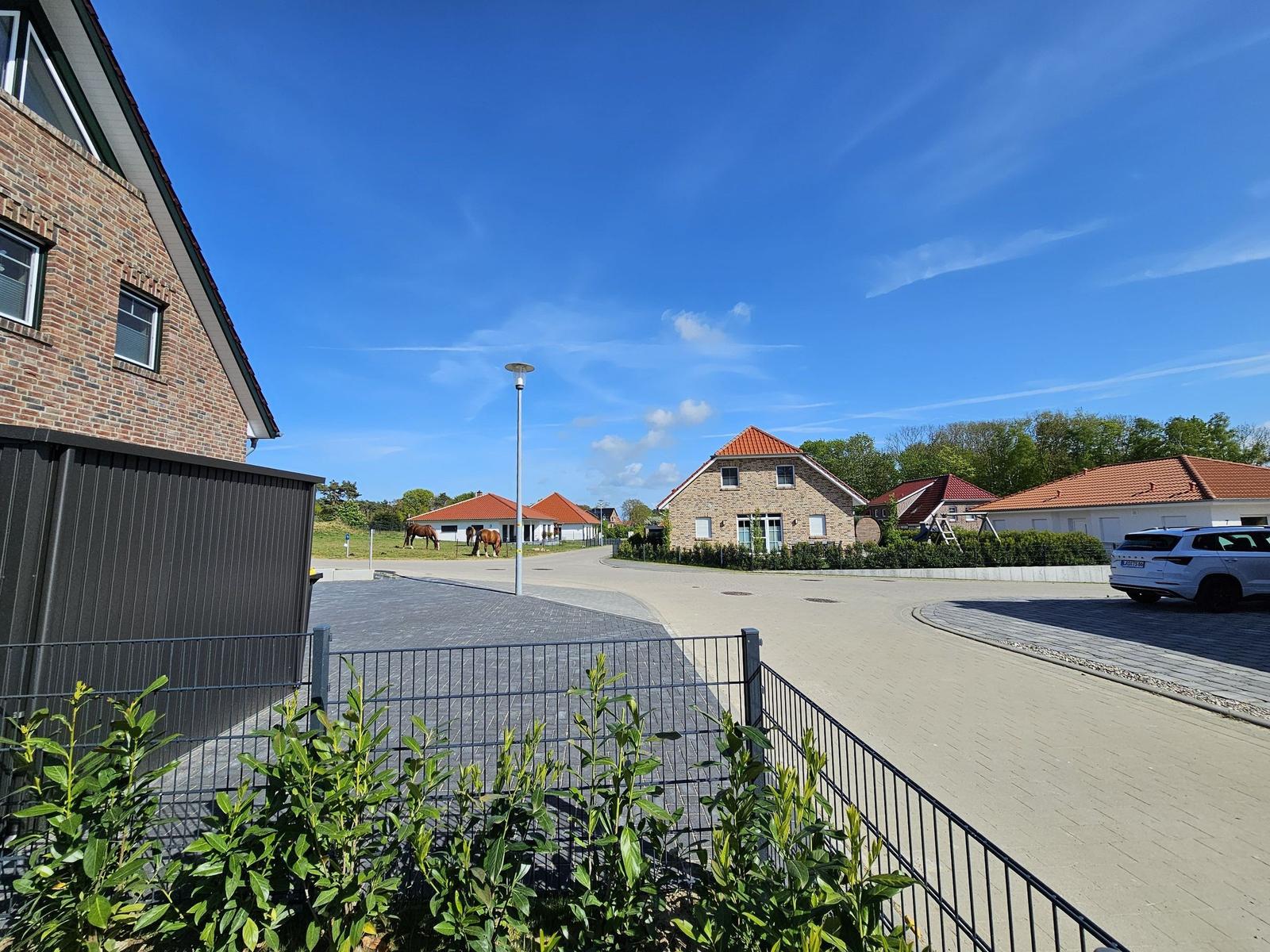 Haus mit rotem Dach, gepflasterter Weg und Grünflächen unter blauem Himmel.