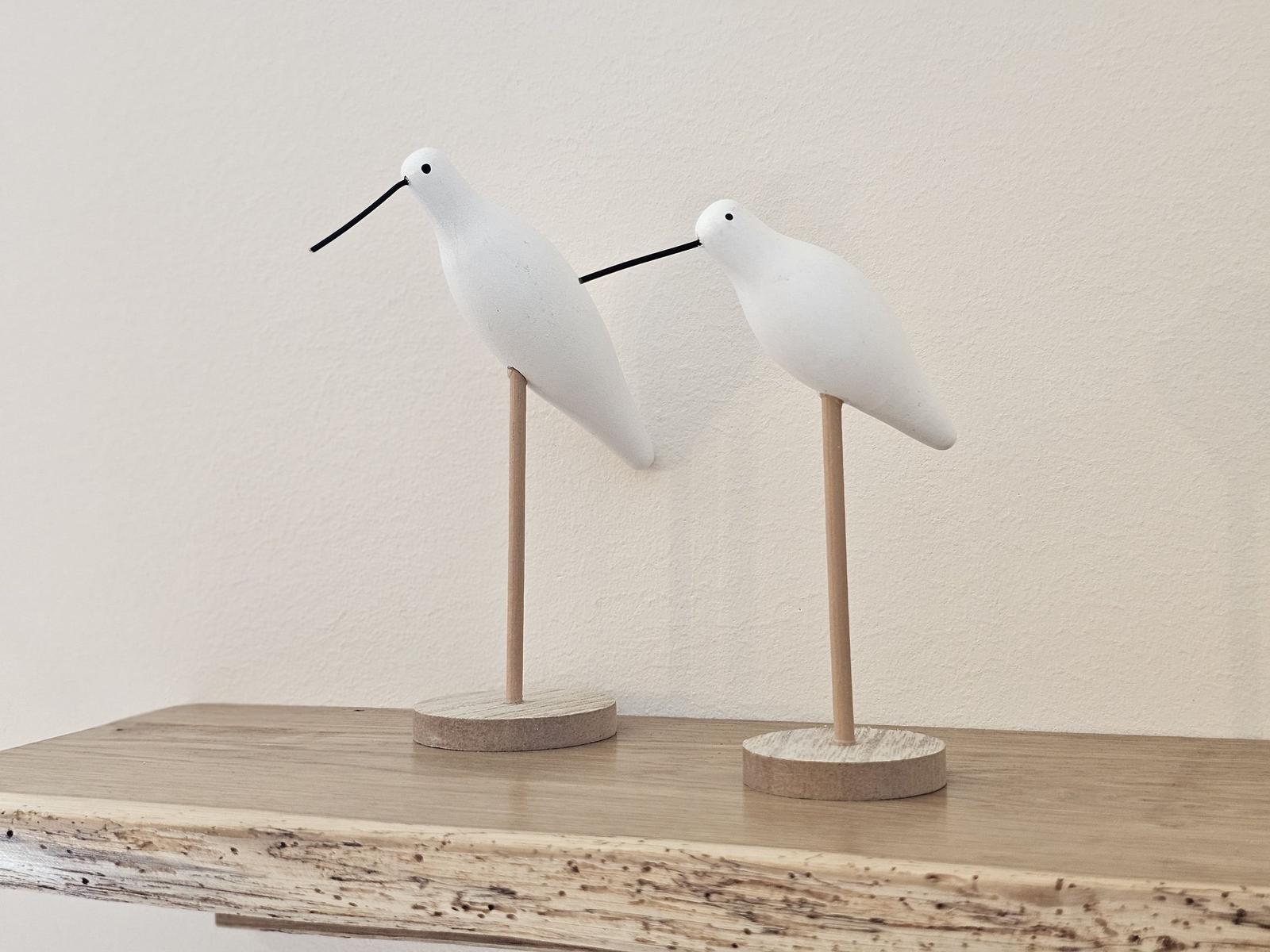 Zwei weiße Vogel-Dekorationsobjekte auf einem Holzregal.