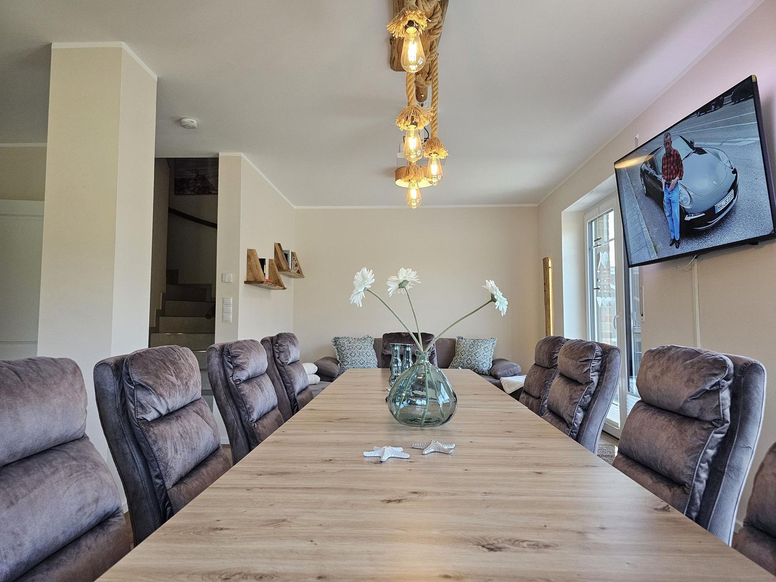 Esszimmer mit langem Holztisch, Stühlen und Fernseher an der Wand.