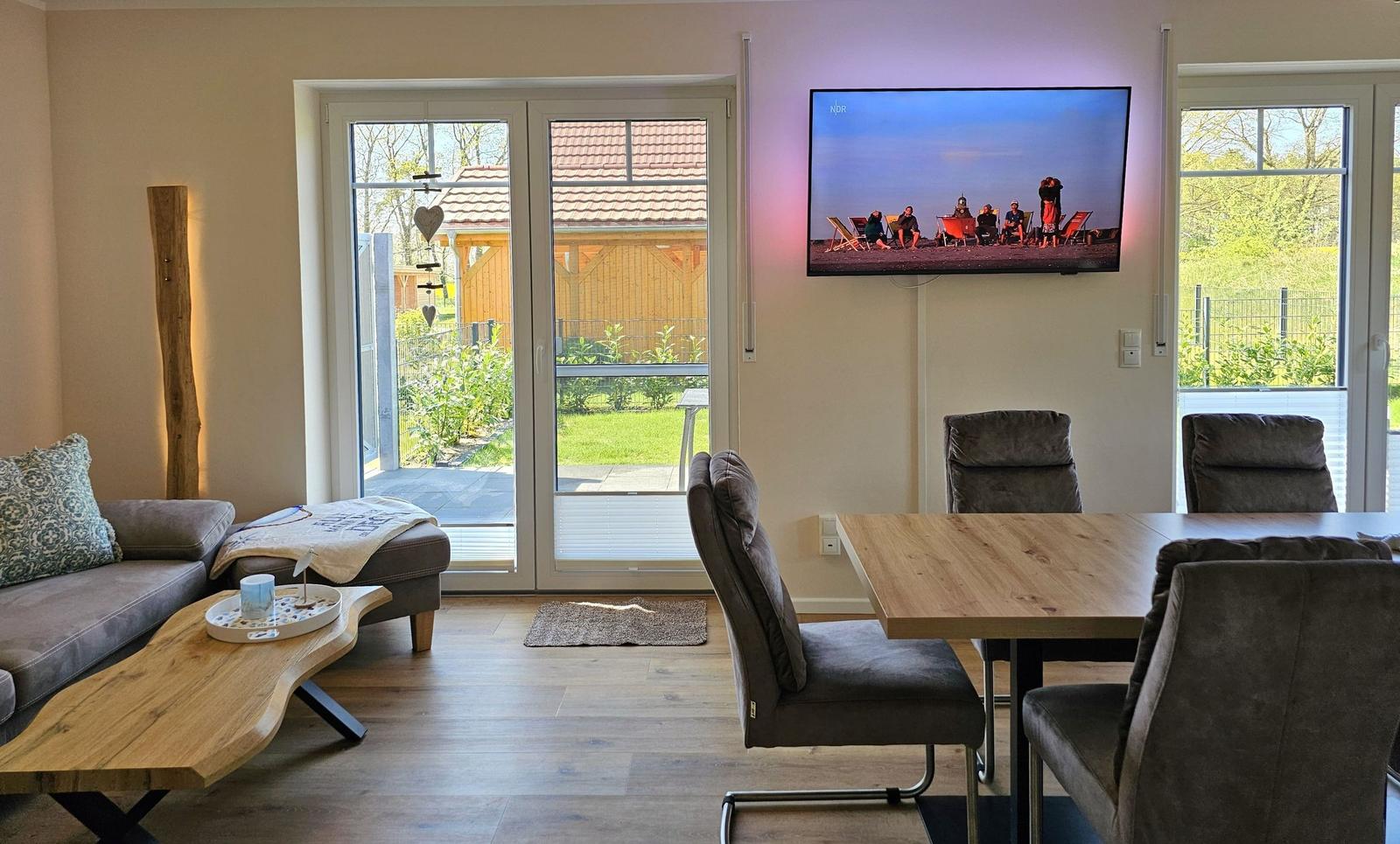 Wohn- und Essbereich mit Fernseher, Sitzgelegenheiten und Blick auf Garten.