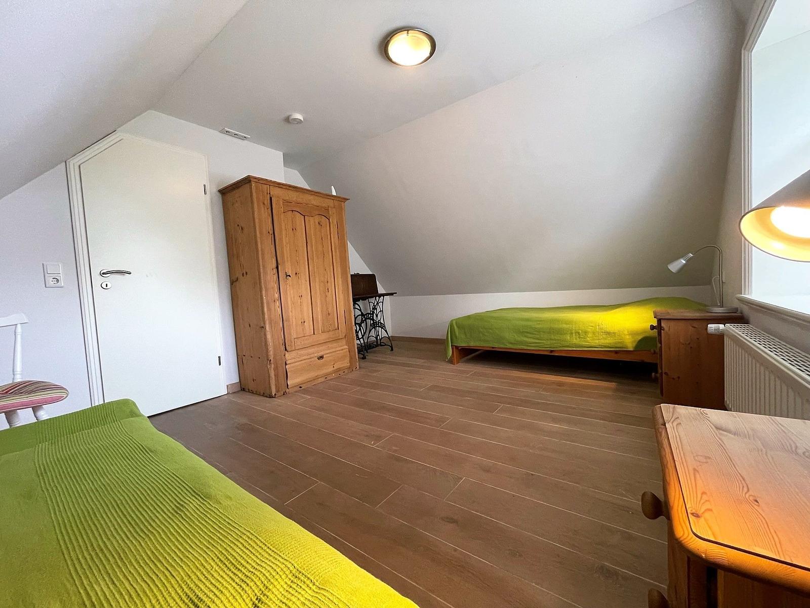 Schlafzimmer mit grünem Bett, Holzmöbeln und Holzboden unter schrägem Dach
