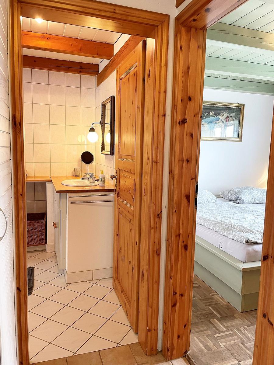 Badezimmer mit Waschbecken und Spiegel. Nebenraum mit Bett und Wandbild.