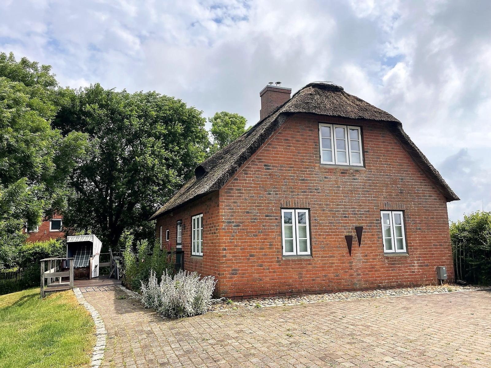 Rotes Backsteingebäude mit Strohdach und weißen Fenstern. Gartenweg und Badehaus im Hintergrund.