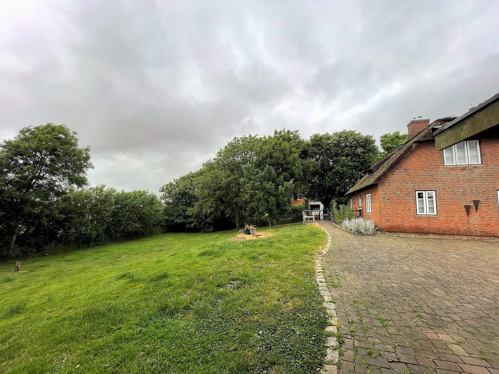 Roter Backsteinbau mit strohgedecktem Dach, umgeben von Grünfläche und Bäumen.