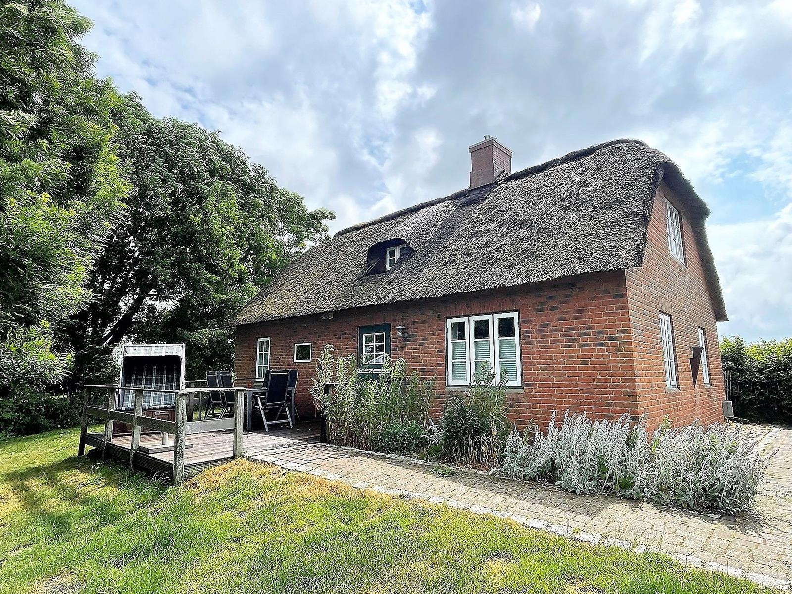 Rotes Backsteingebäude mit Strohdach, Terrasse und Garten. 