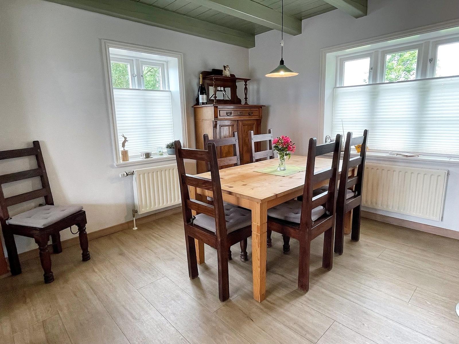 Esszimmer mit Holztisch, Stühlen und Fenstern. Holzfußboden und Deckenbalken.