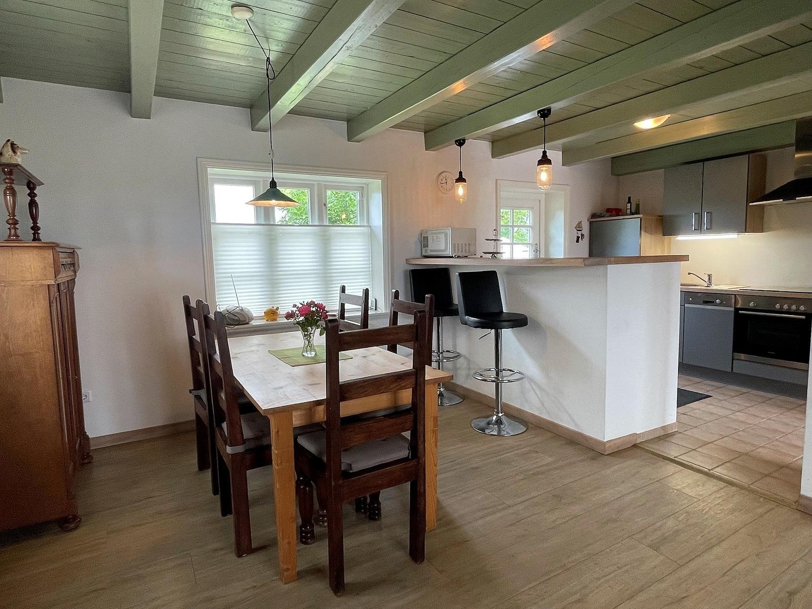 Essbereich mit Tisch, Stühlen und Kücheninsel mit Barhockern.