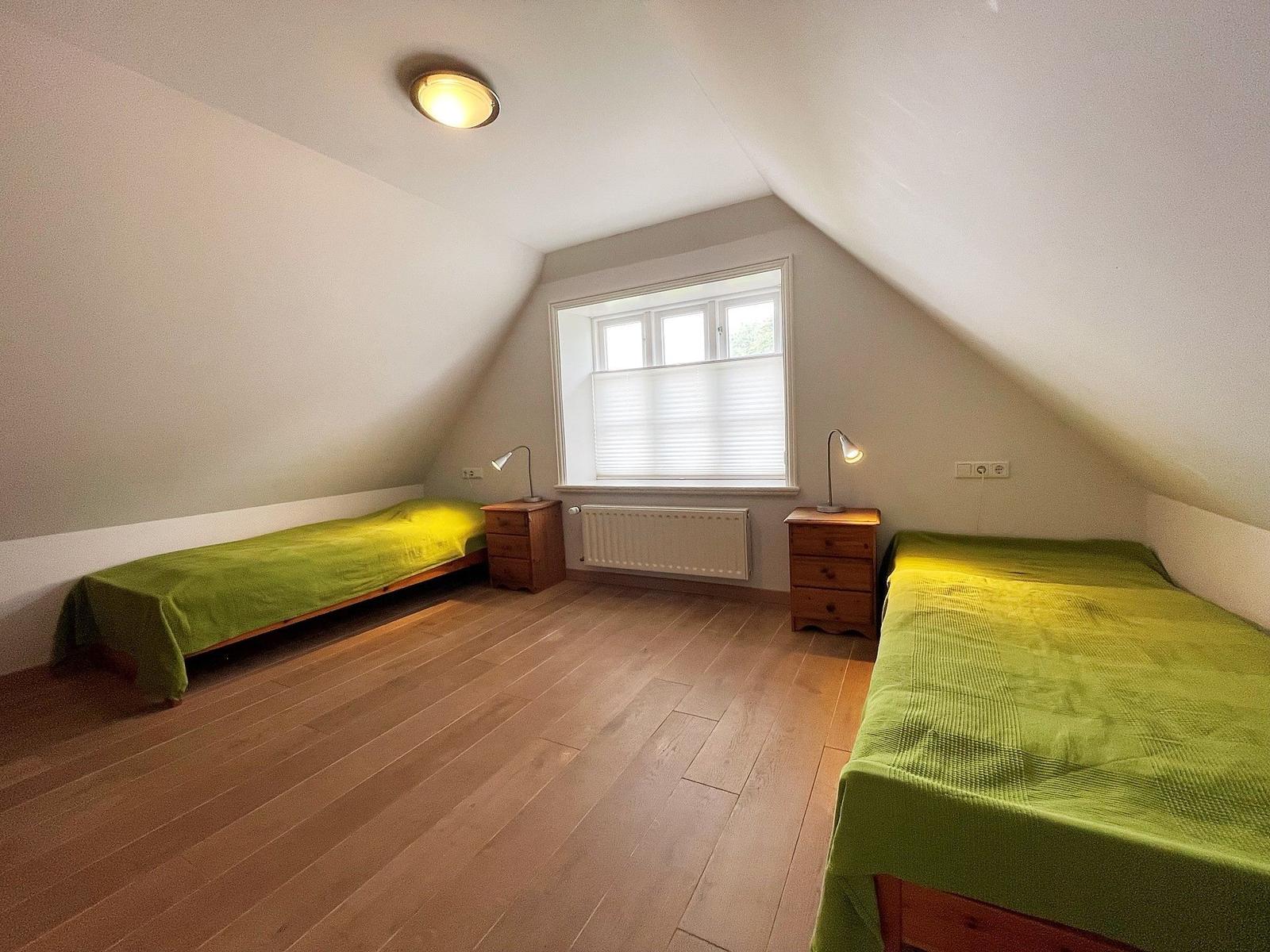 Zwei Betten mit grünen Bettdecken, Holzboden und schrägem Dach