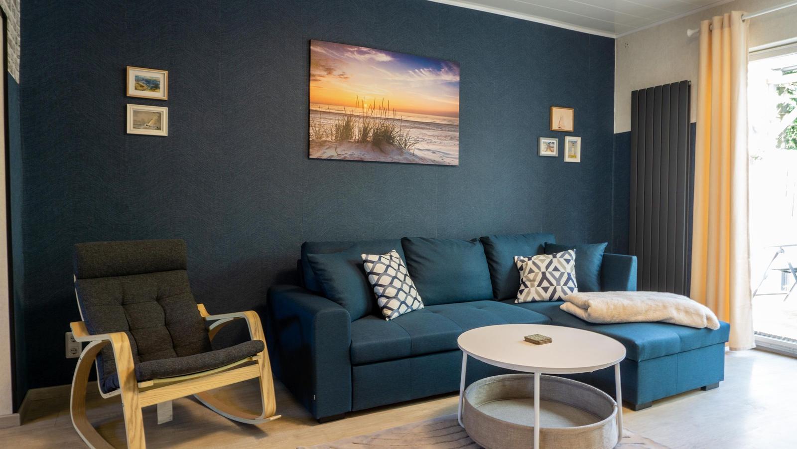 Ein Wohnzimmer mit blauem Sofa, einem Schaukelstuhl und einer Wanddekoration.