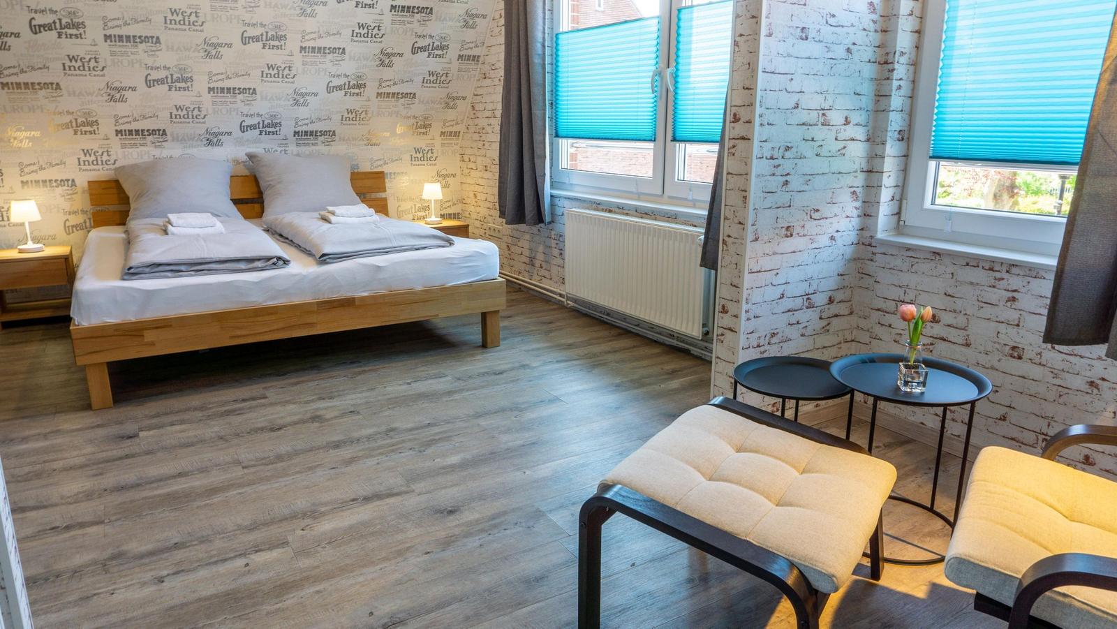 Schlafzimmer mit Doppelbett, Holzboden und Fenstern mit Jalousien.