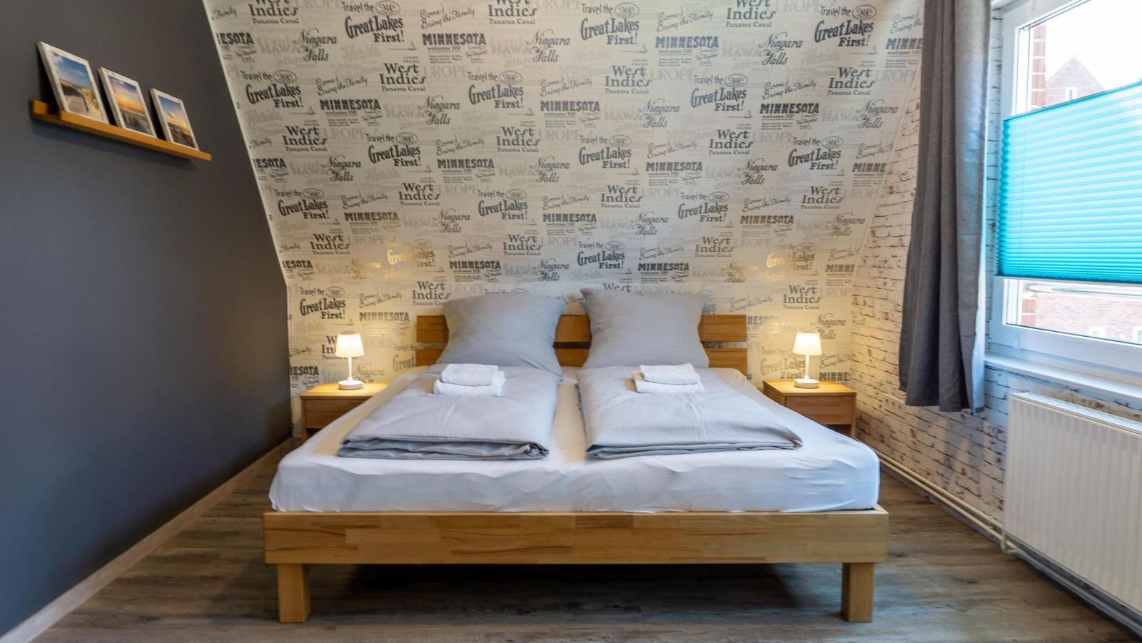 Schlafzimmer mit Doppelbett, Textildruckwand und Holzmöbeln.