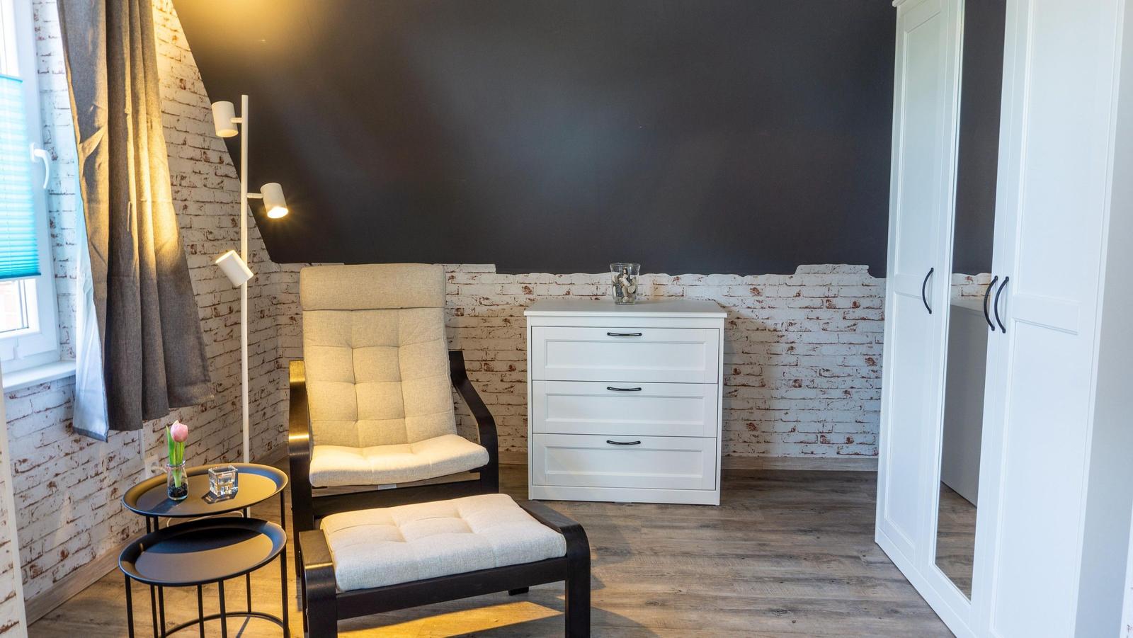 Schlafzimmer mit Stuhl, Nachttisch, Schrank und weißem Schrank.