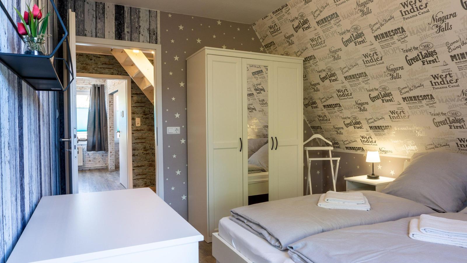 Schlafzimmer mit Doppelbett, Kleiderschrank und Wand mit Reiseaufdrucken.