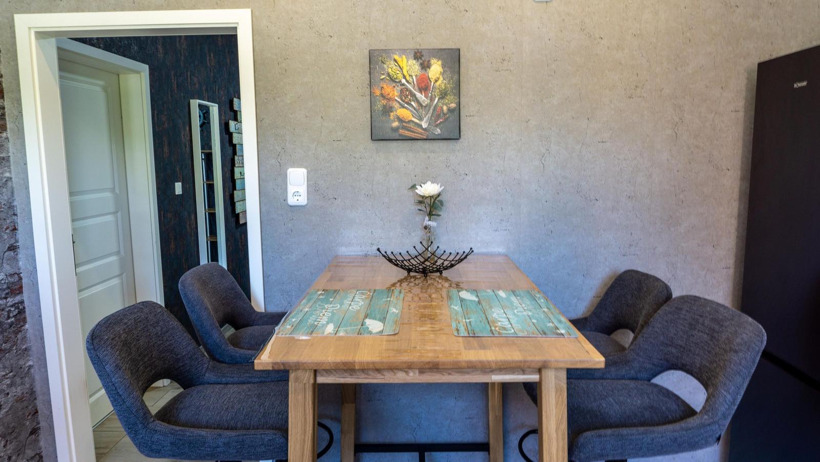 Essbereich mit Holztisch, vier Stühlen und Wandbild.