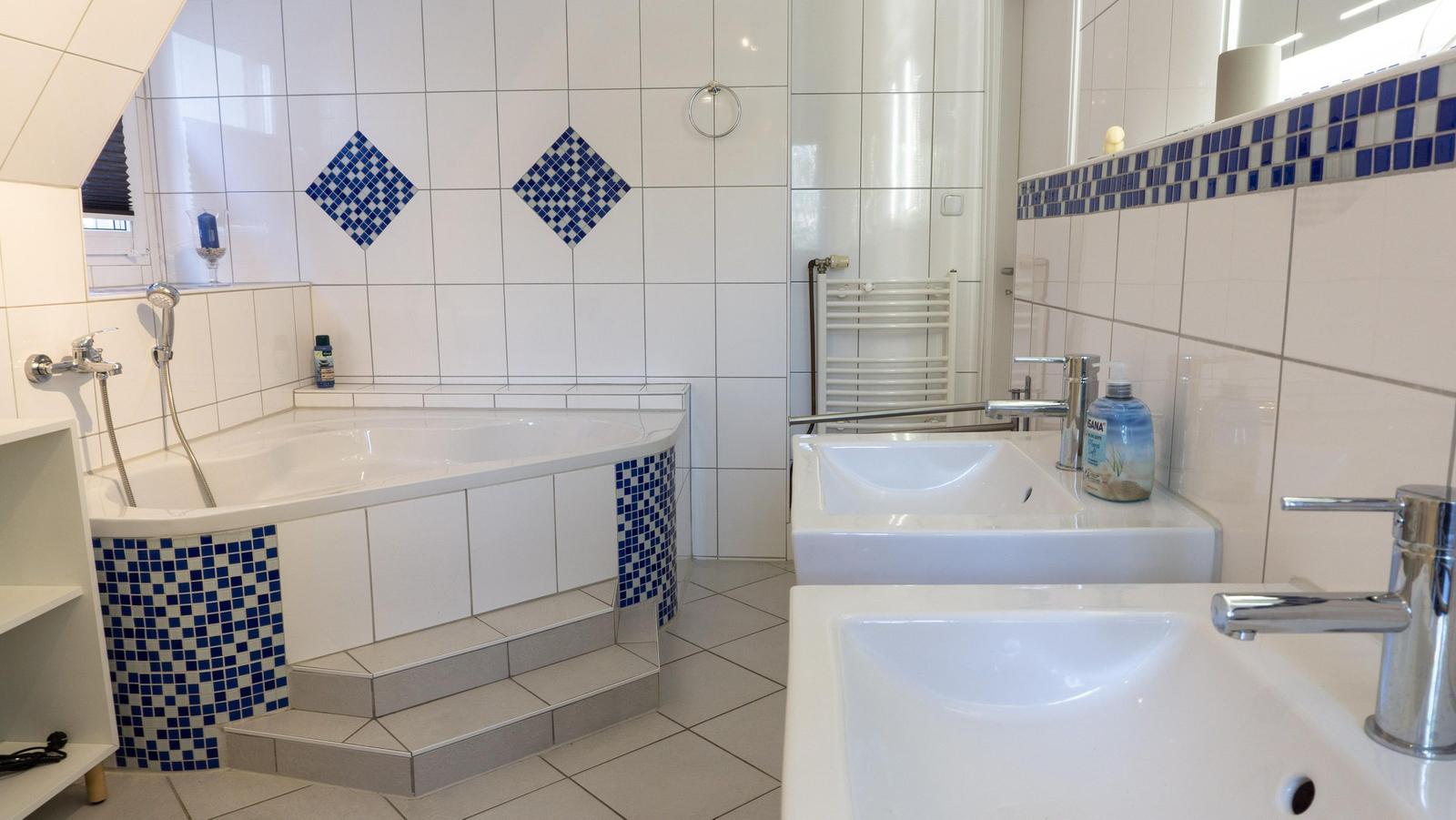 Badezimmer mit Badewanne, zwei Waschbecken und blauen Mosaikfliesen an den Wänden.