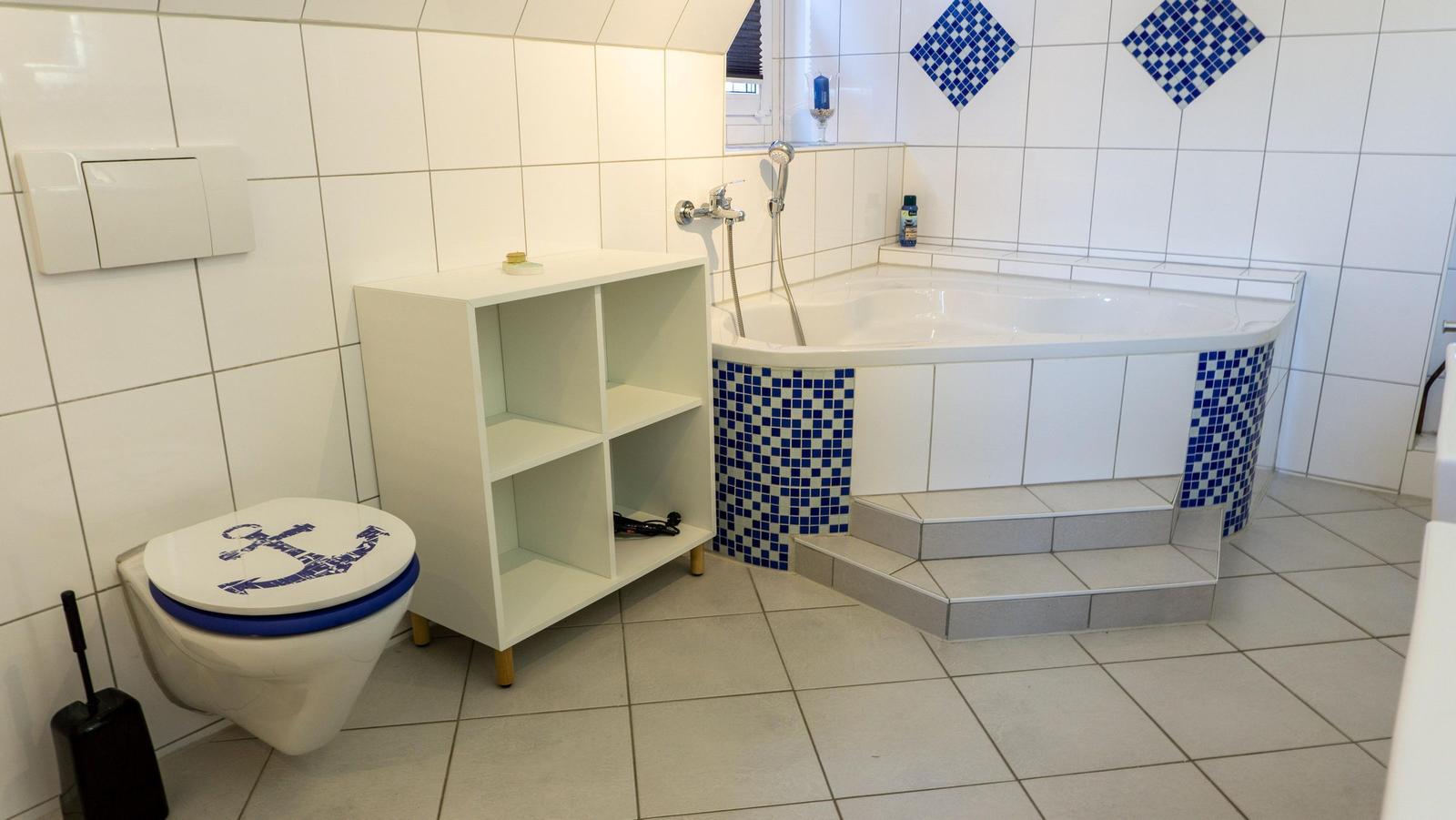 Badezimmer mit Badewanne, Toilette und Regal. Blaue Mosaikfliesen an der Wand.