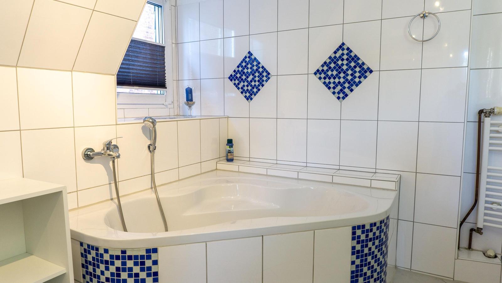 Bad mit Whirlpool, blauen Mosaikfliesen und Fenster mit Jalousie.