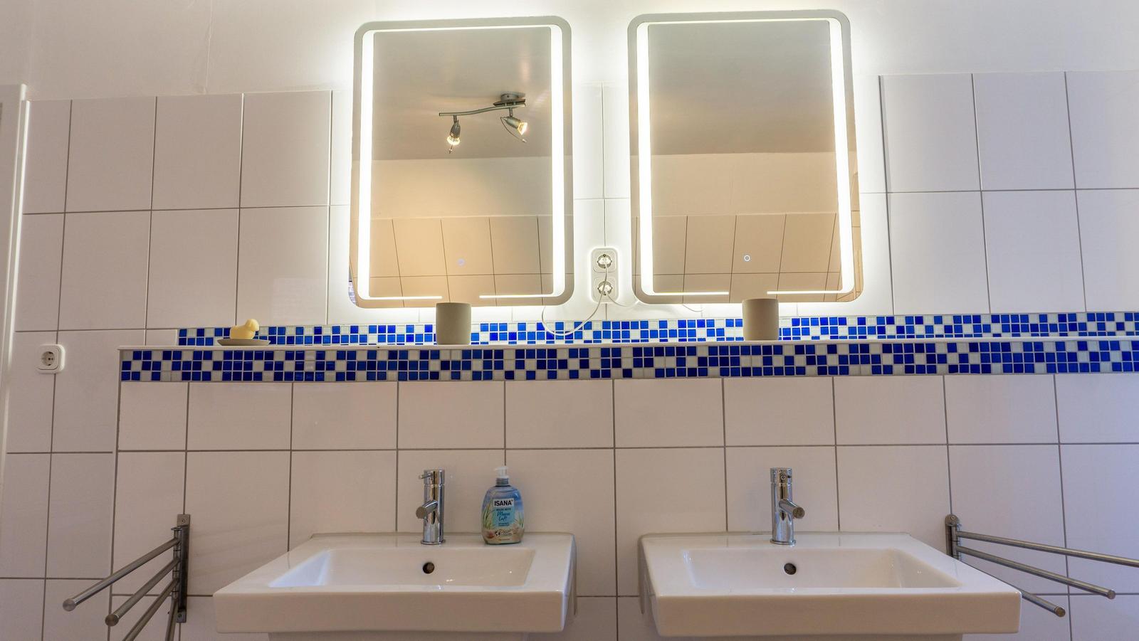 Zwei Waschbecken mit beleuchteten Spiegeln und blau-weißem Fliesenspiegel.