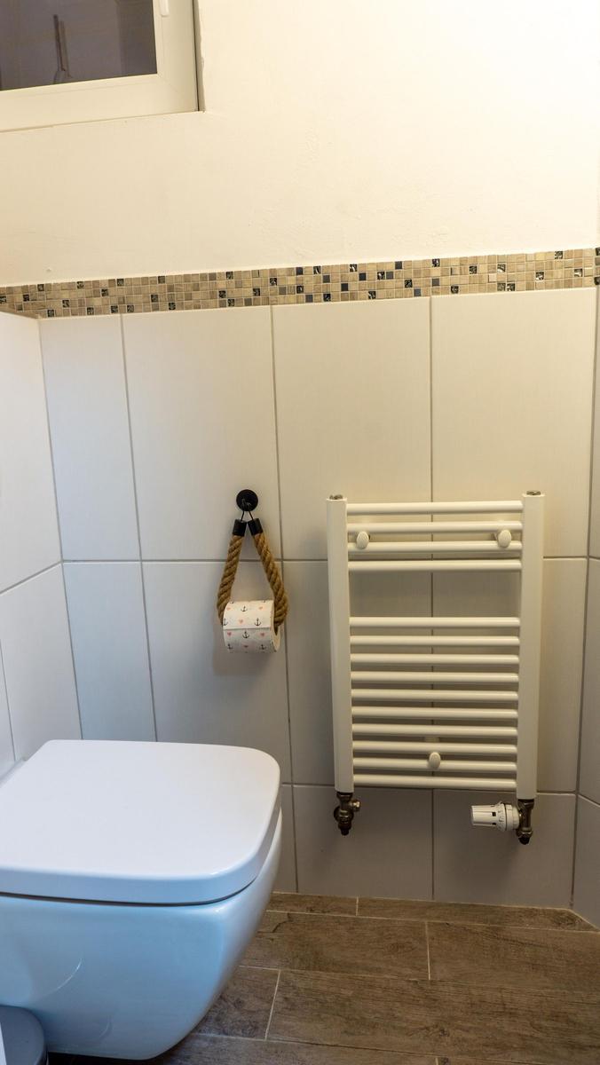 Badezimmer mit Toilette, Heizkörper und Toilettenpapierhalter.