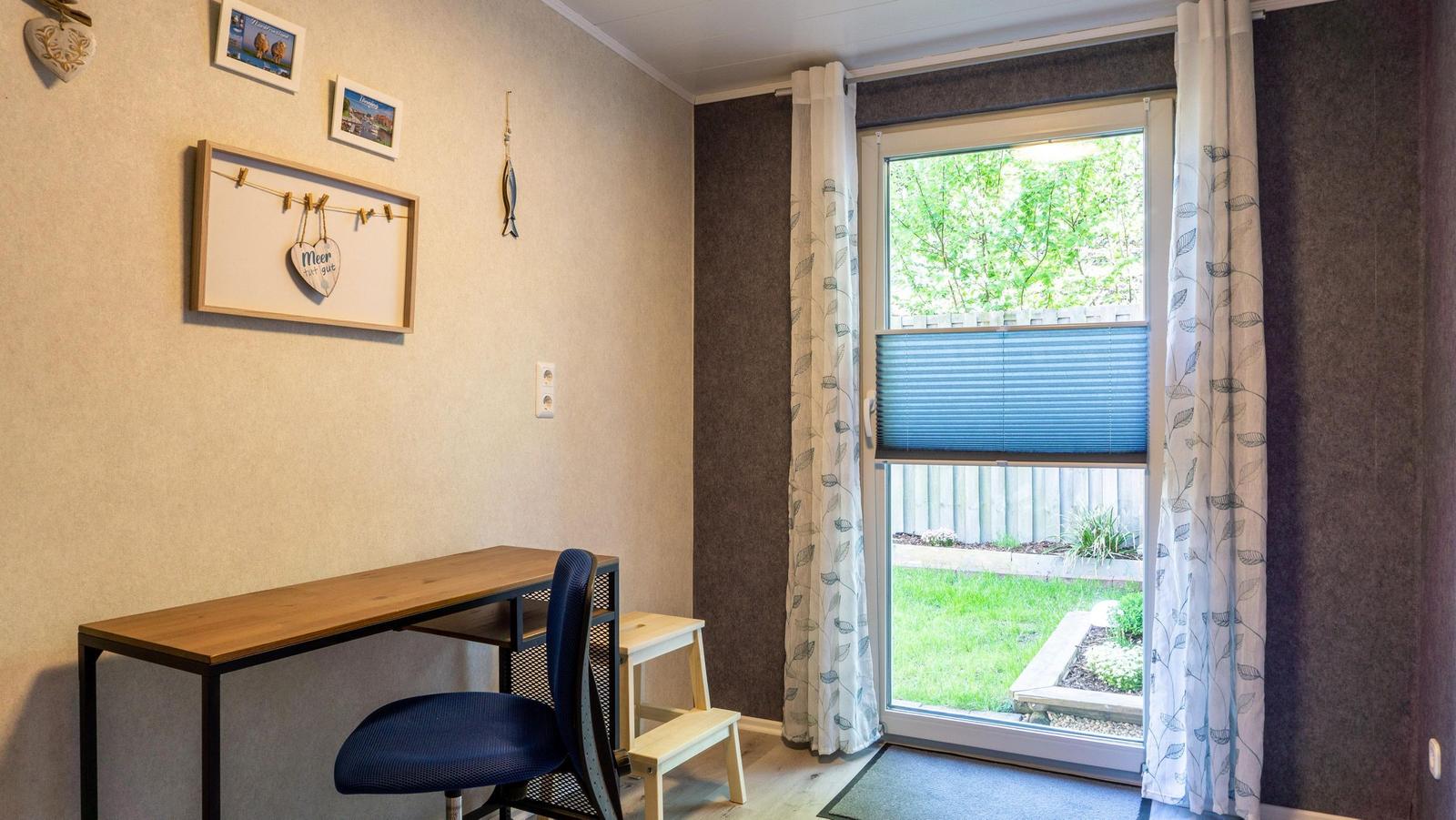 Schreibtisch mit Stuhl und Fensterblick auf Garten.