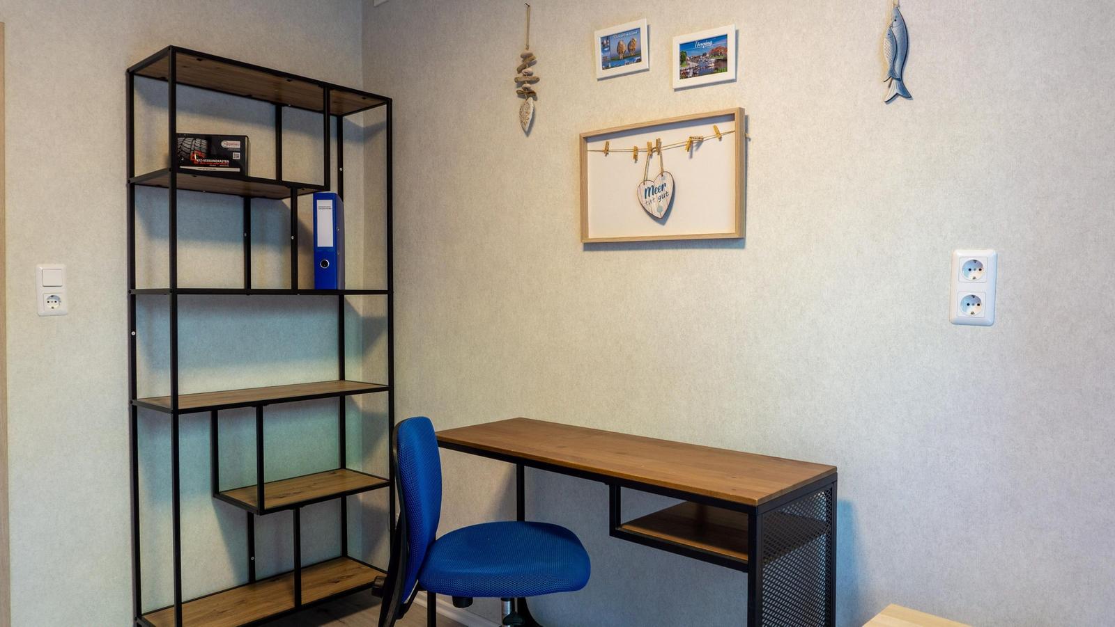 Arbeitszimmer mit Schreibtisch, blauer Stuhl und Regal an der Wand.
