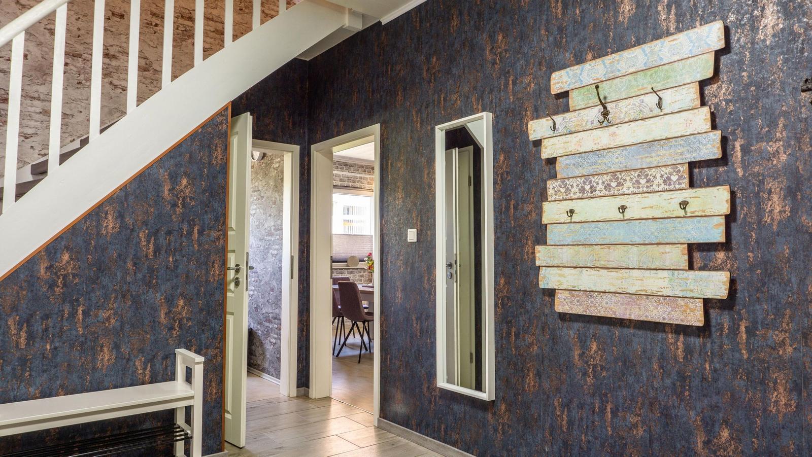 Eingangsbereich mit dunkler Tapete, Holzbank, Wandgarderobe und Treppenhaus.