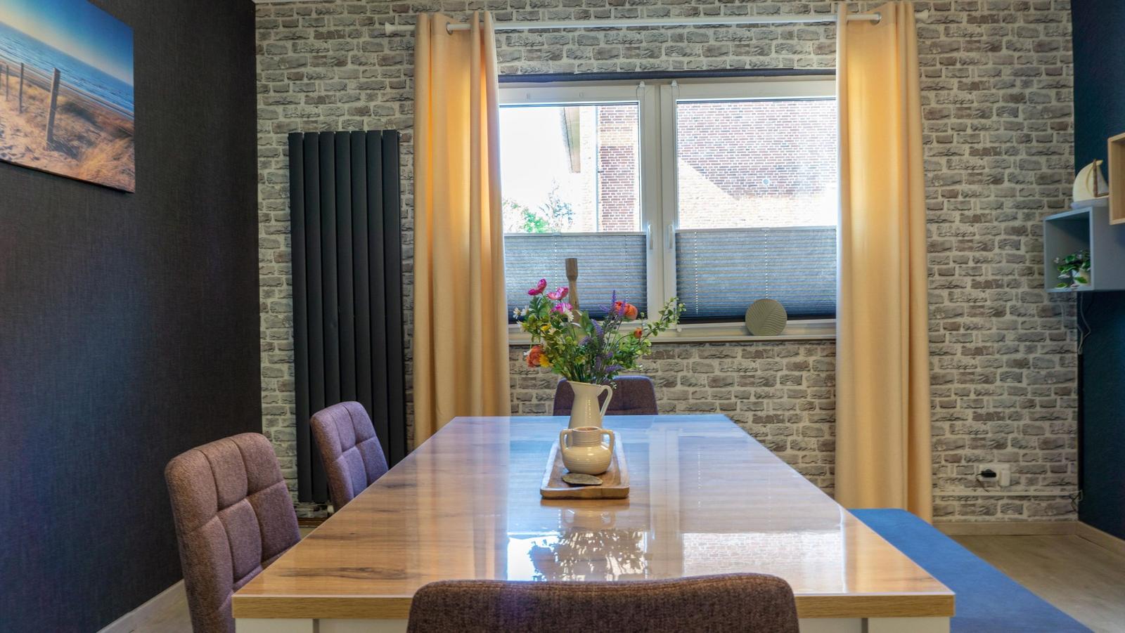 Esszimmer mit Holztisch, Stühlen und Fenster mit Vorhängen.