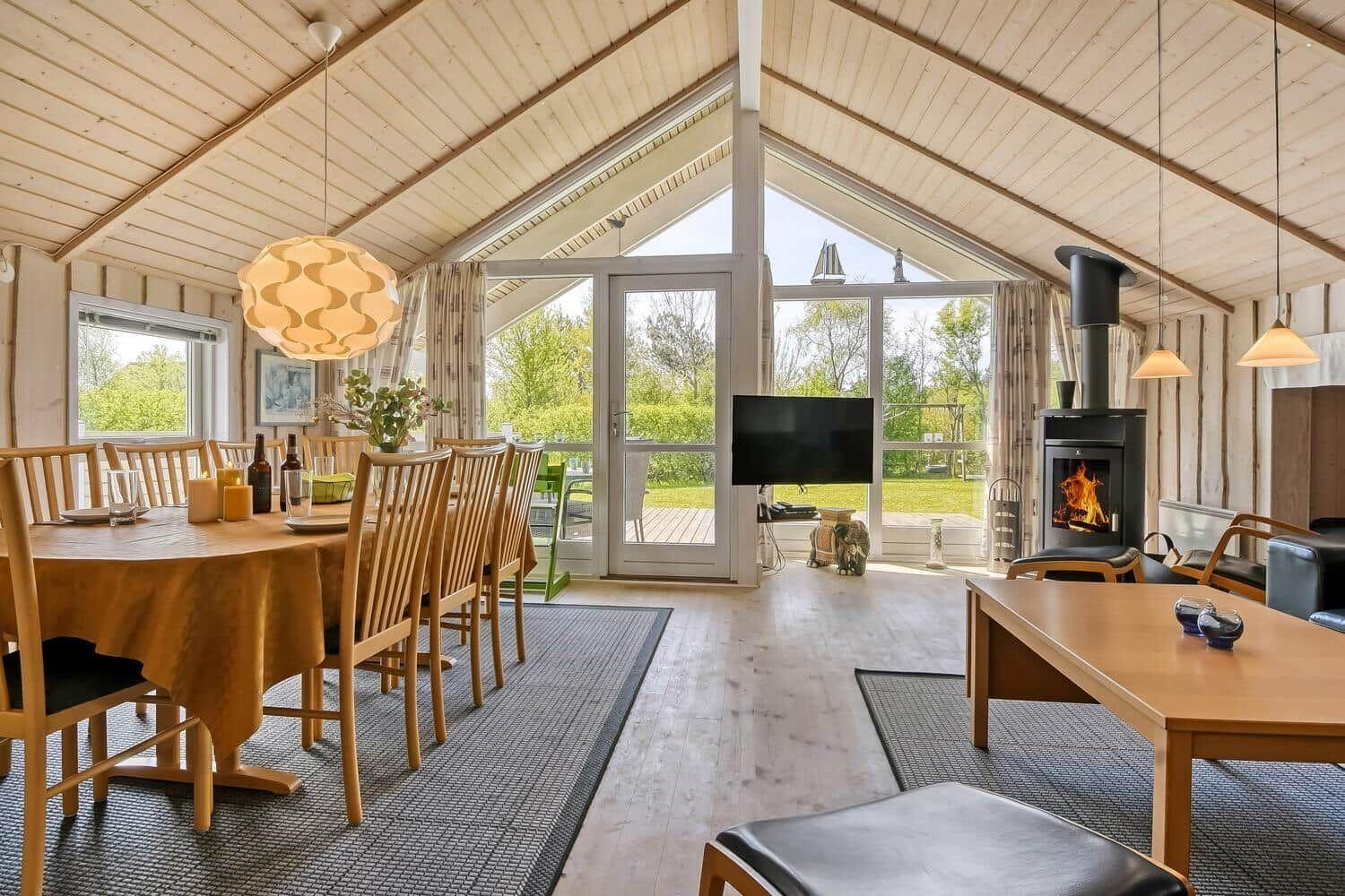 Großes Wohn- und Esszimmer mit Holzdecke, Kamin und Glastüren zur Terrasse.