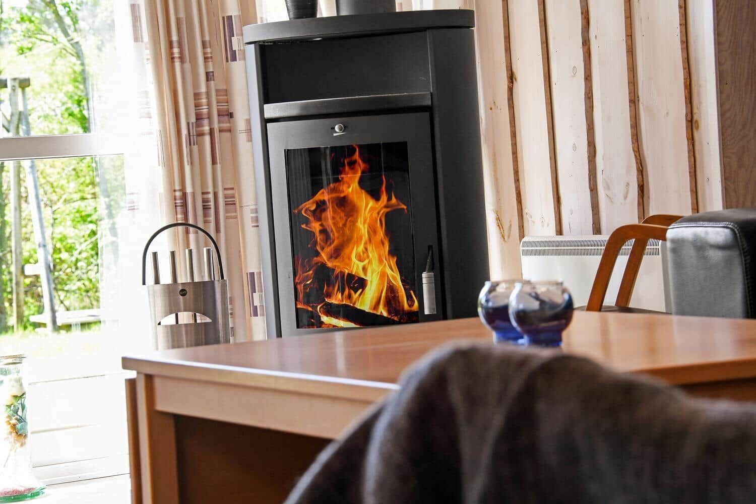 Kaminofen mit brennendem Feuer, Holztisch und Stühle im Raum mit Holzwand.