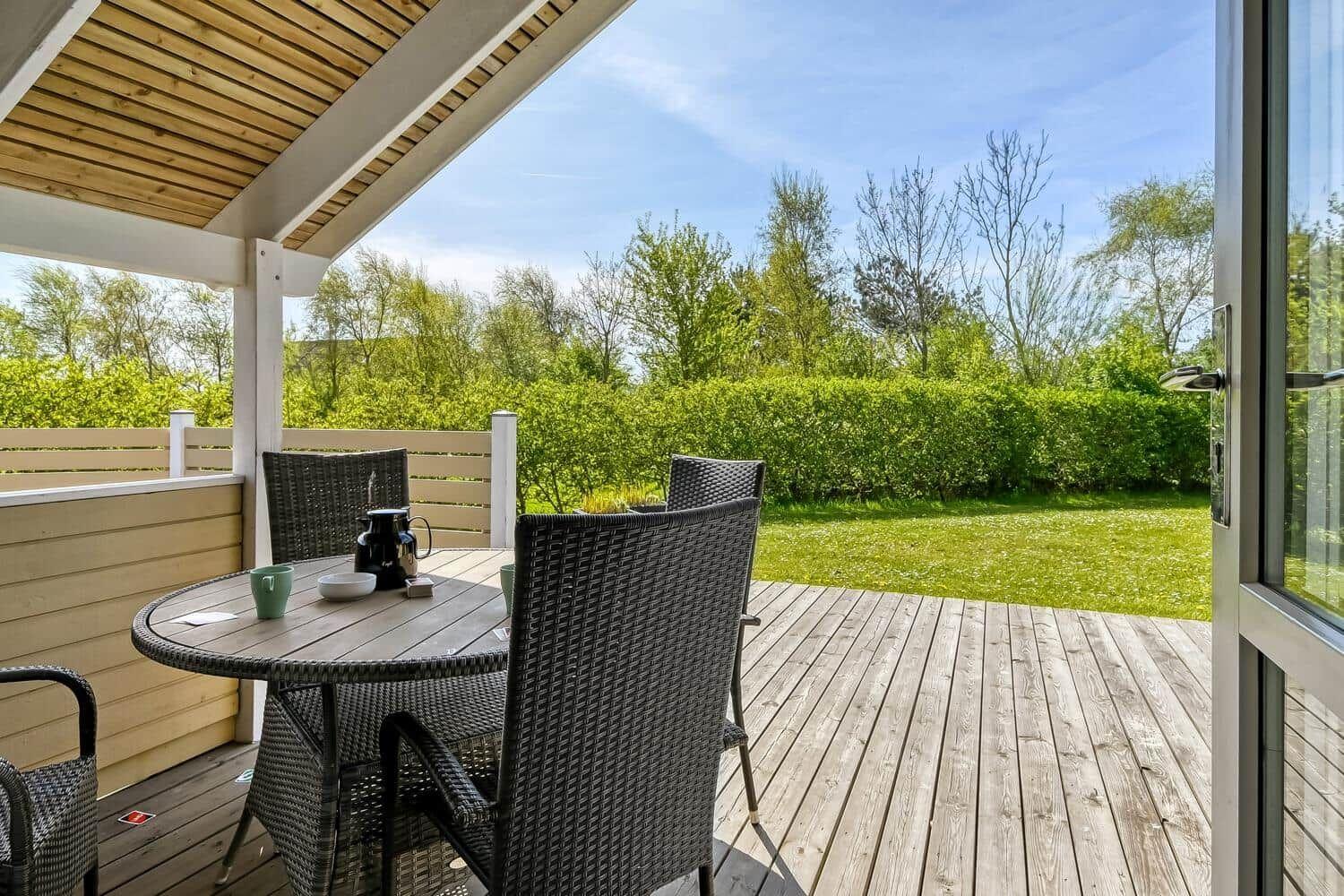 Terrasse mit Tisch und Stühlen, Blick auf grünen Garten und Bäume.