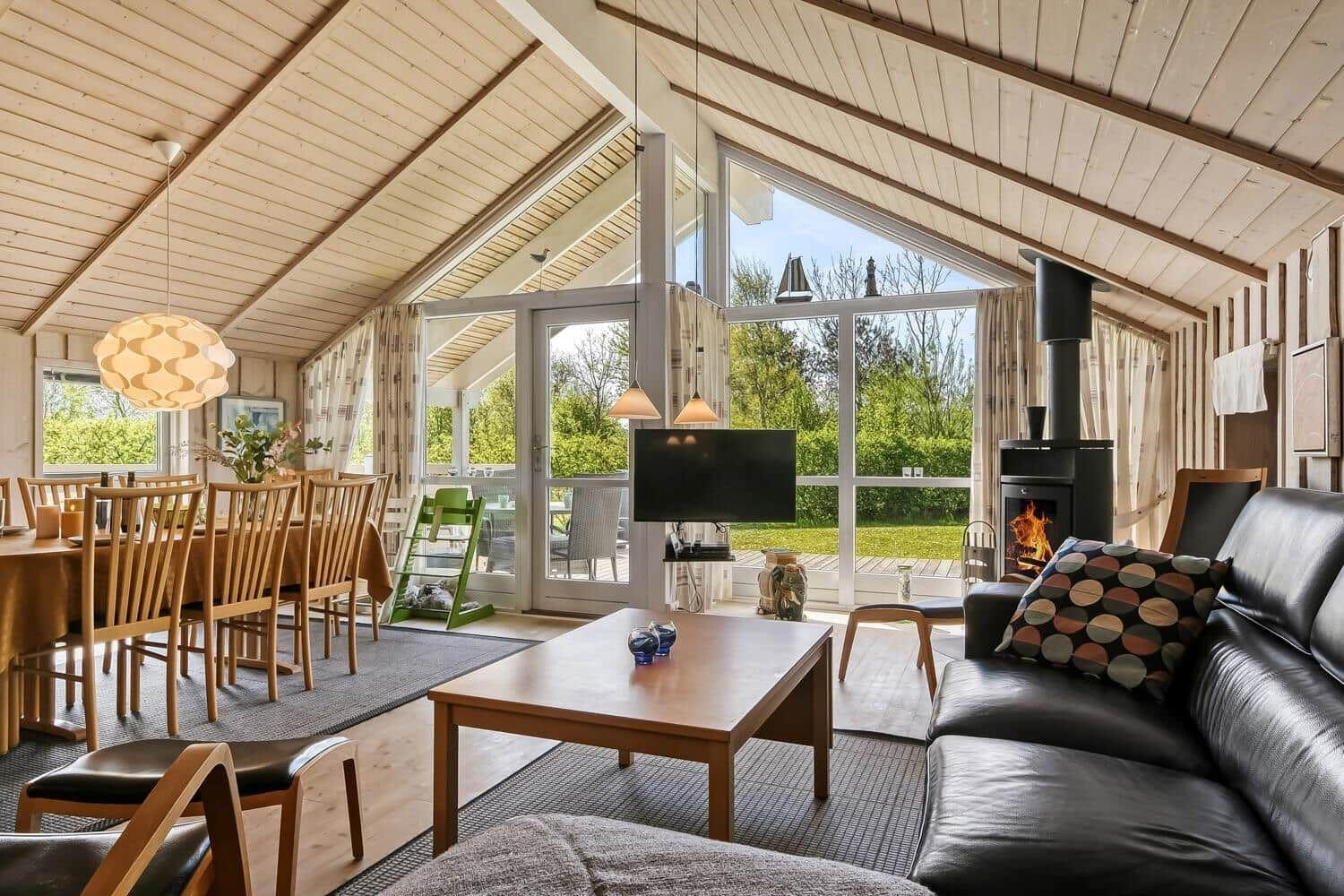 Wohn- und Essbereich mit Holzdecke, Kamin und großem Fensterblick.