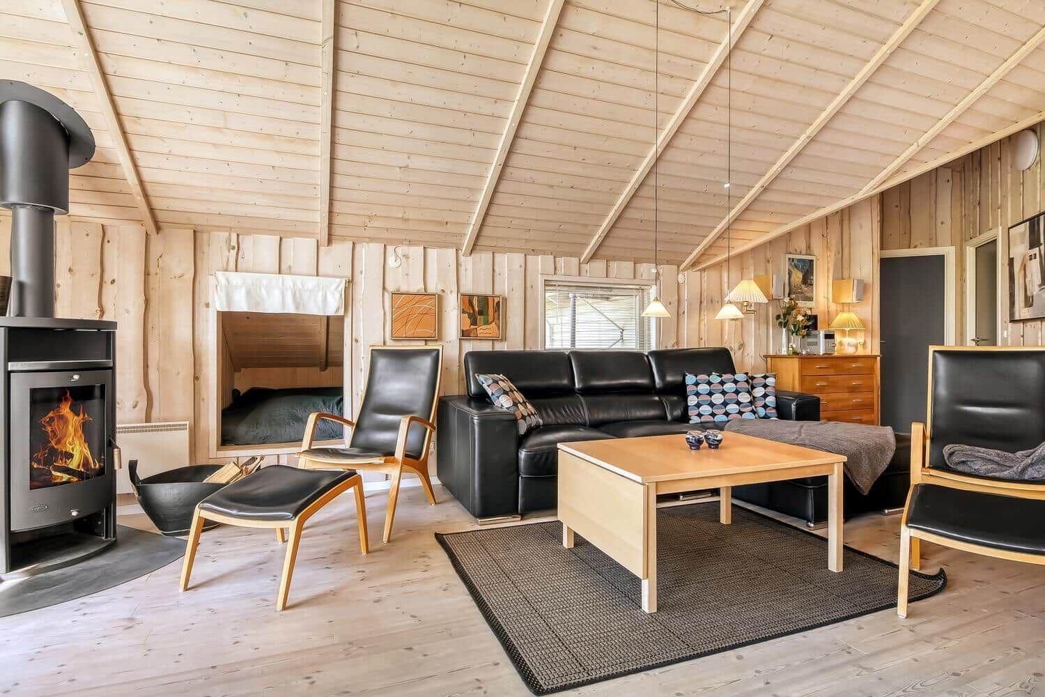 Wohnraum mit Kamin, Sofa, Stühlen und Holzwandverkleidung.
