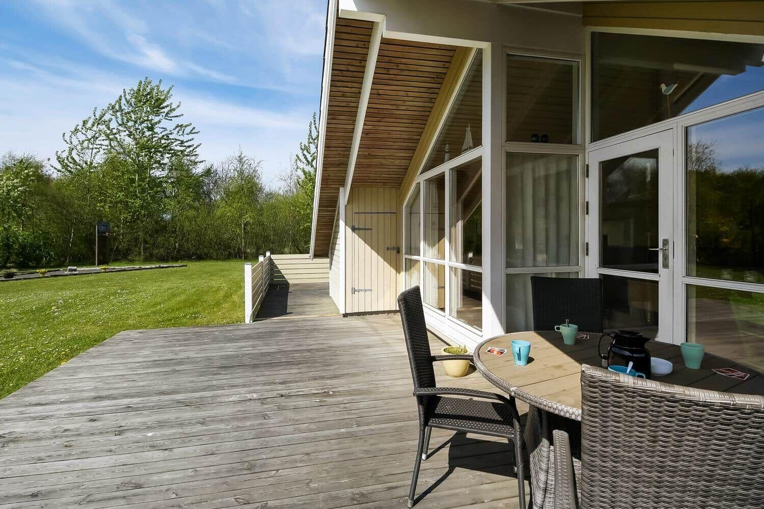 Holzterrasse mit Tisch und Stühlen, Blick auf grünen Rasen und Bäume.