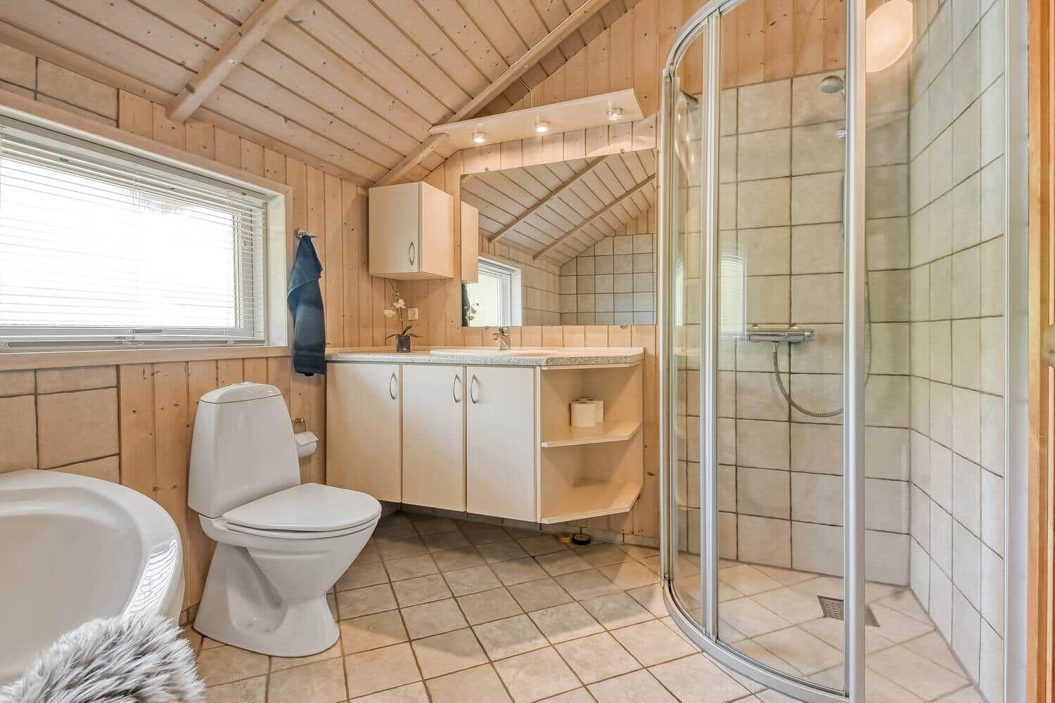 Badezimmer mit Dusche, Waschbecken und Toilette. Holzwände und Fliesenboden.